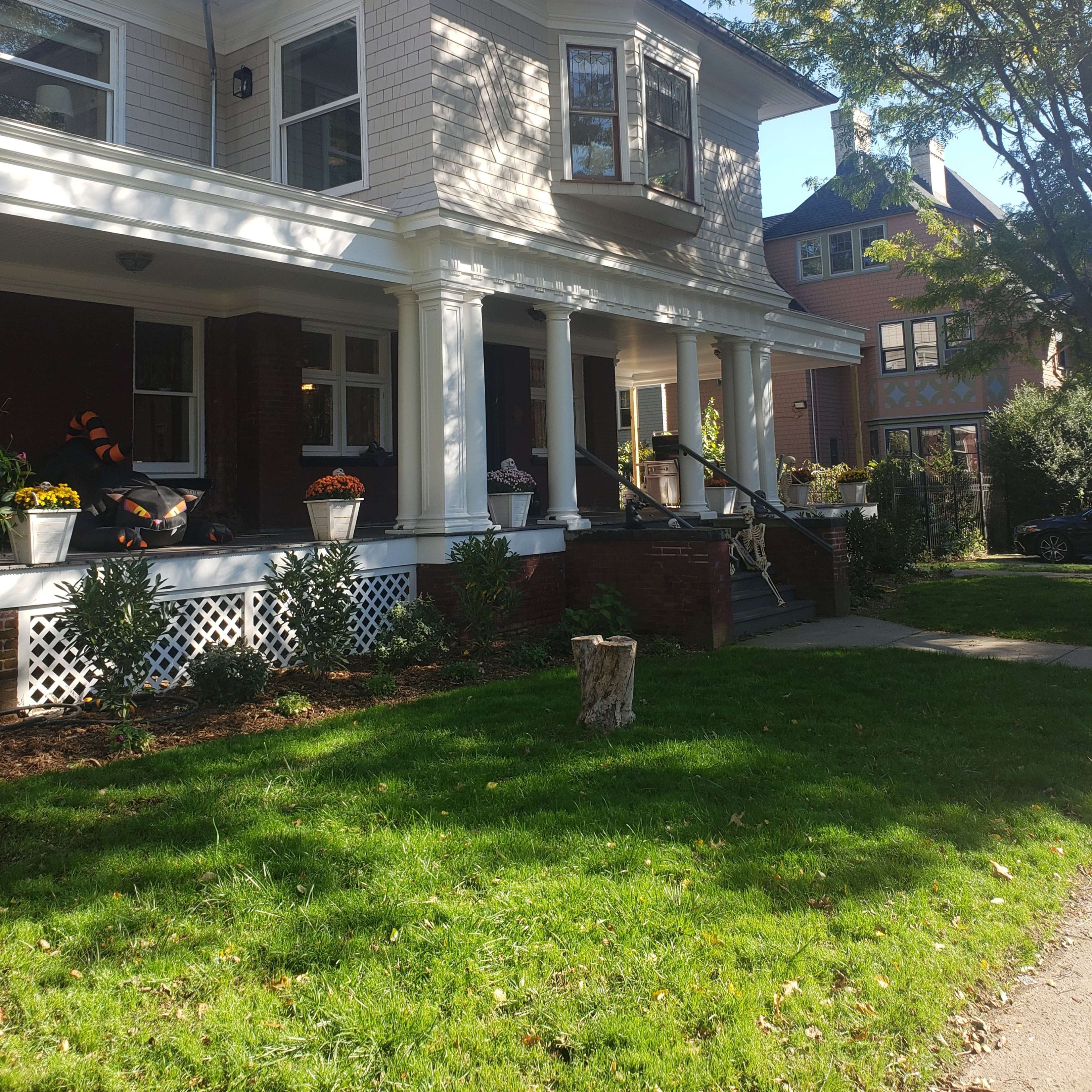 A two-story house with a large porch, surrounded by greenery and other residential buildings nearby.