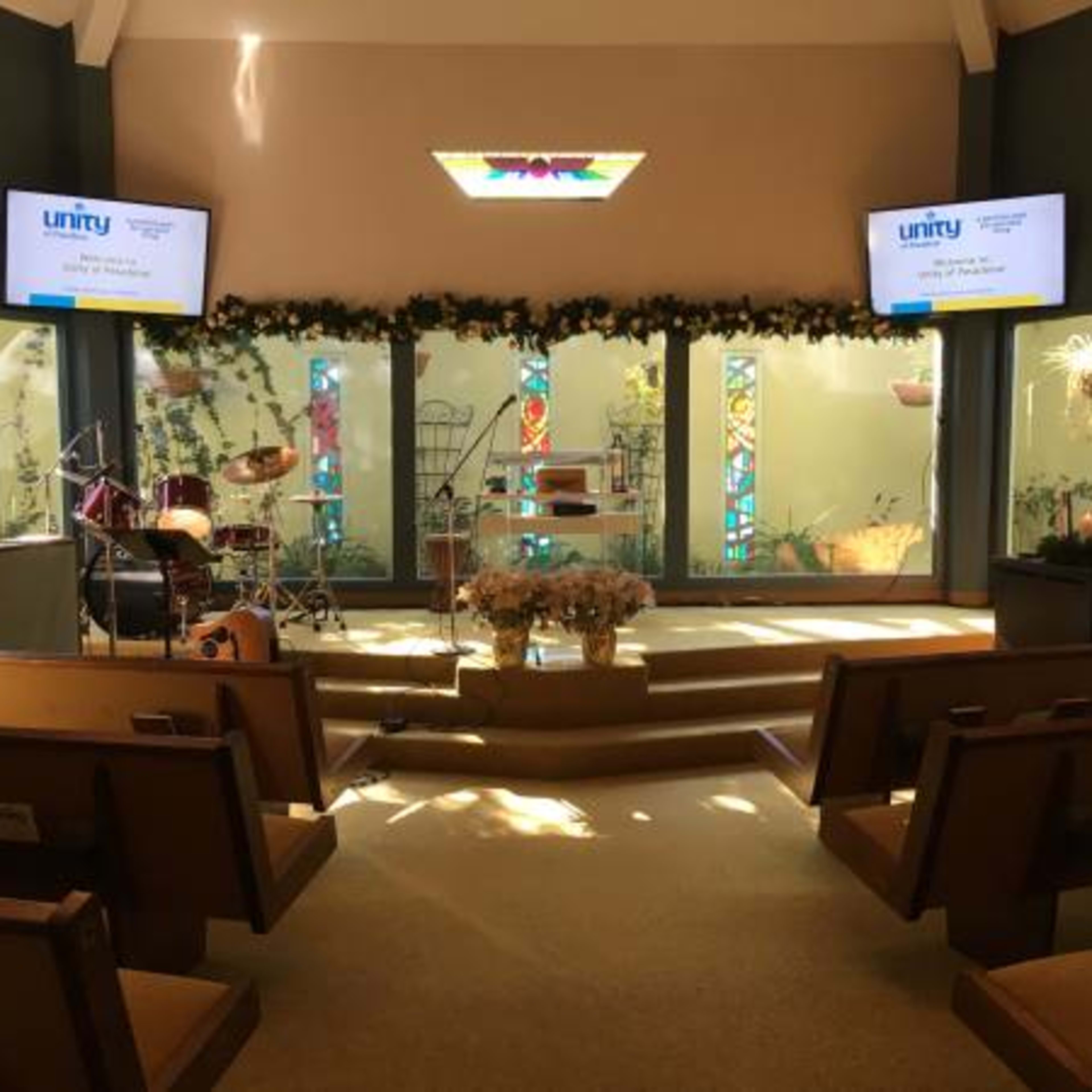 The interior of a church features a stage with musical instruments, bright stained glass windows, and seating arranged in rows.