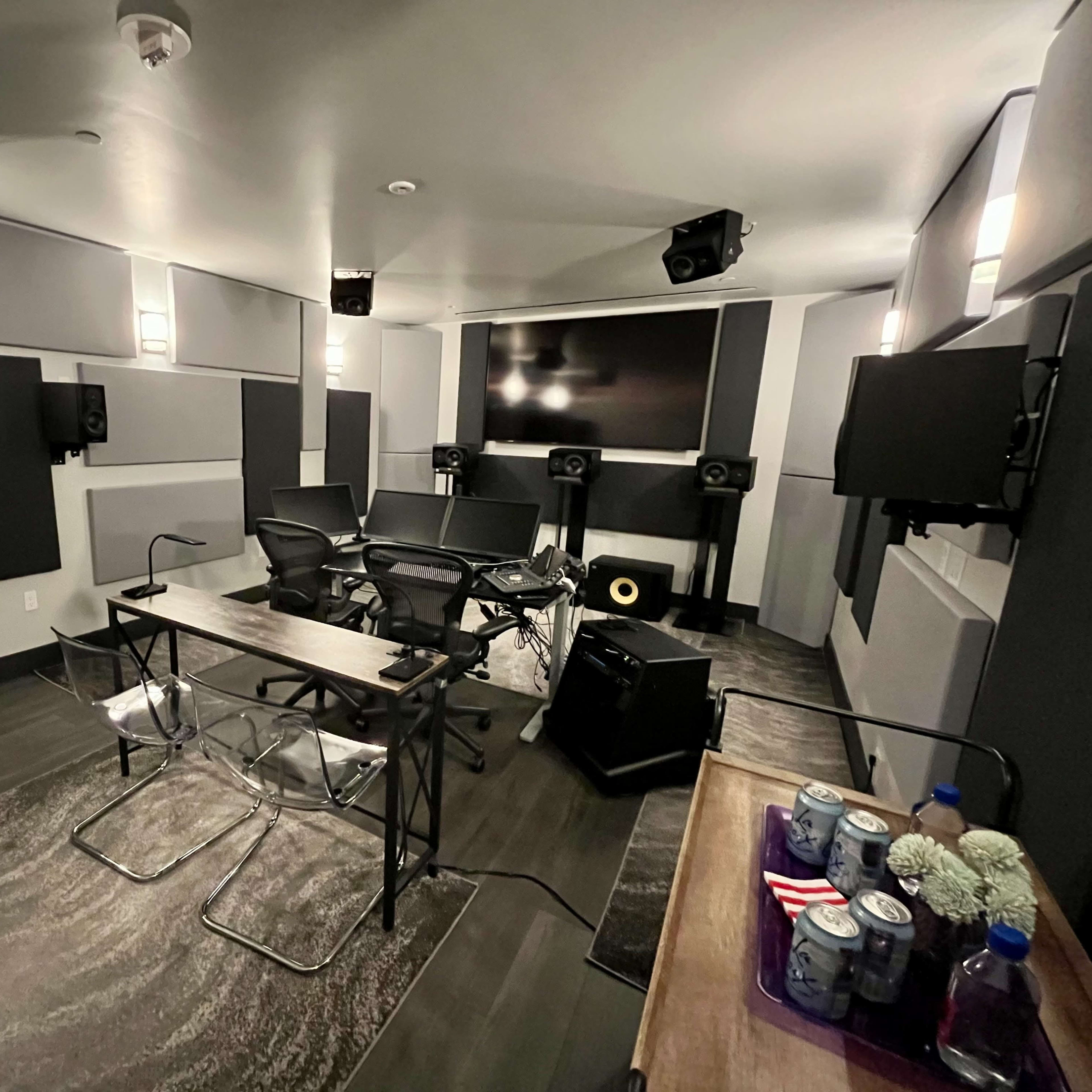 A modern sound studio with soundproofing panels, multiple speakers, and a central workstation featuring chairs and digital screens.