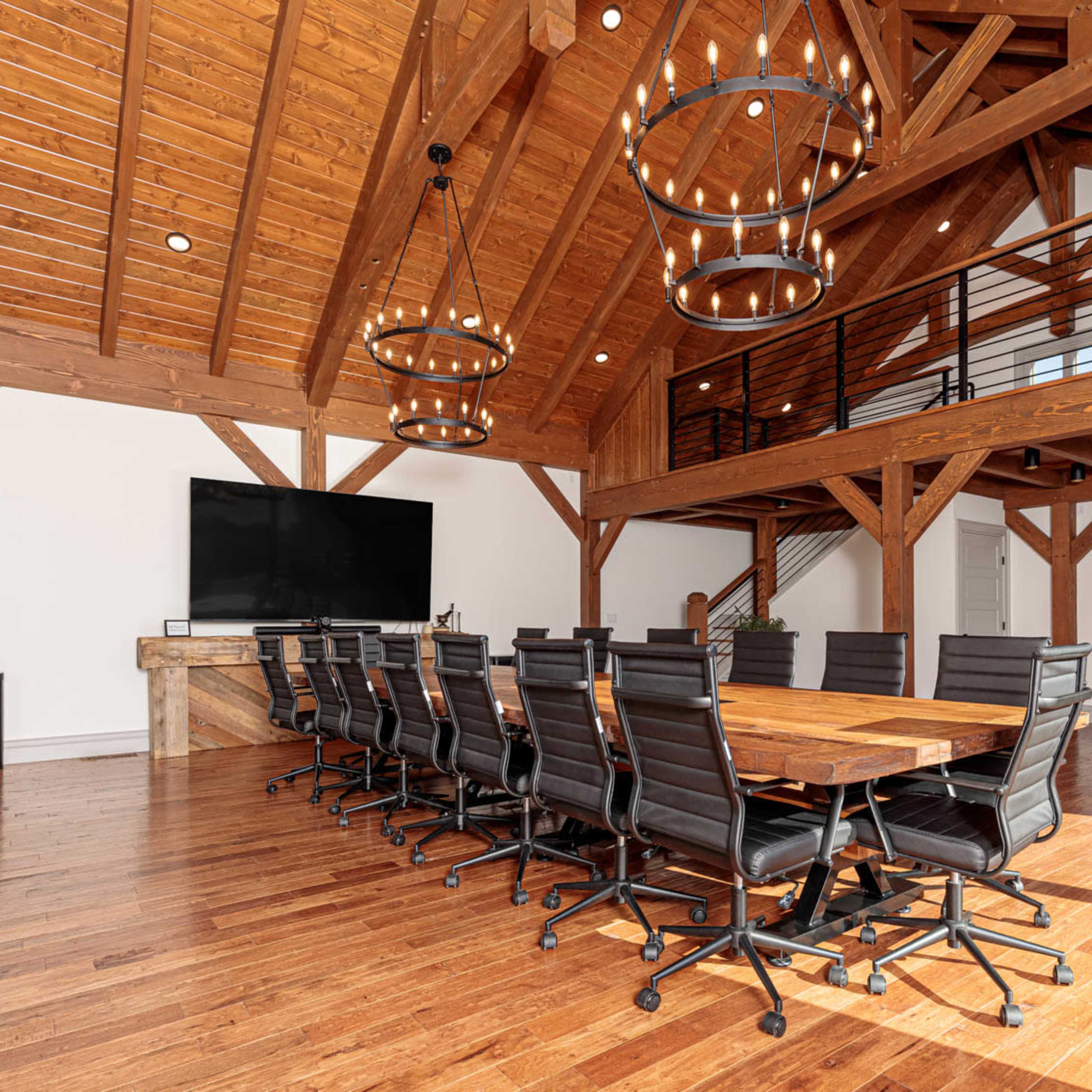 A spacious dining area features a large wooden table surrounded by black chairs, complemented by high wooden beams and circular light fixtures.