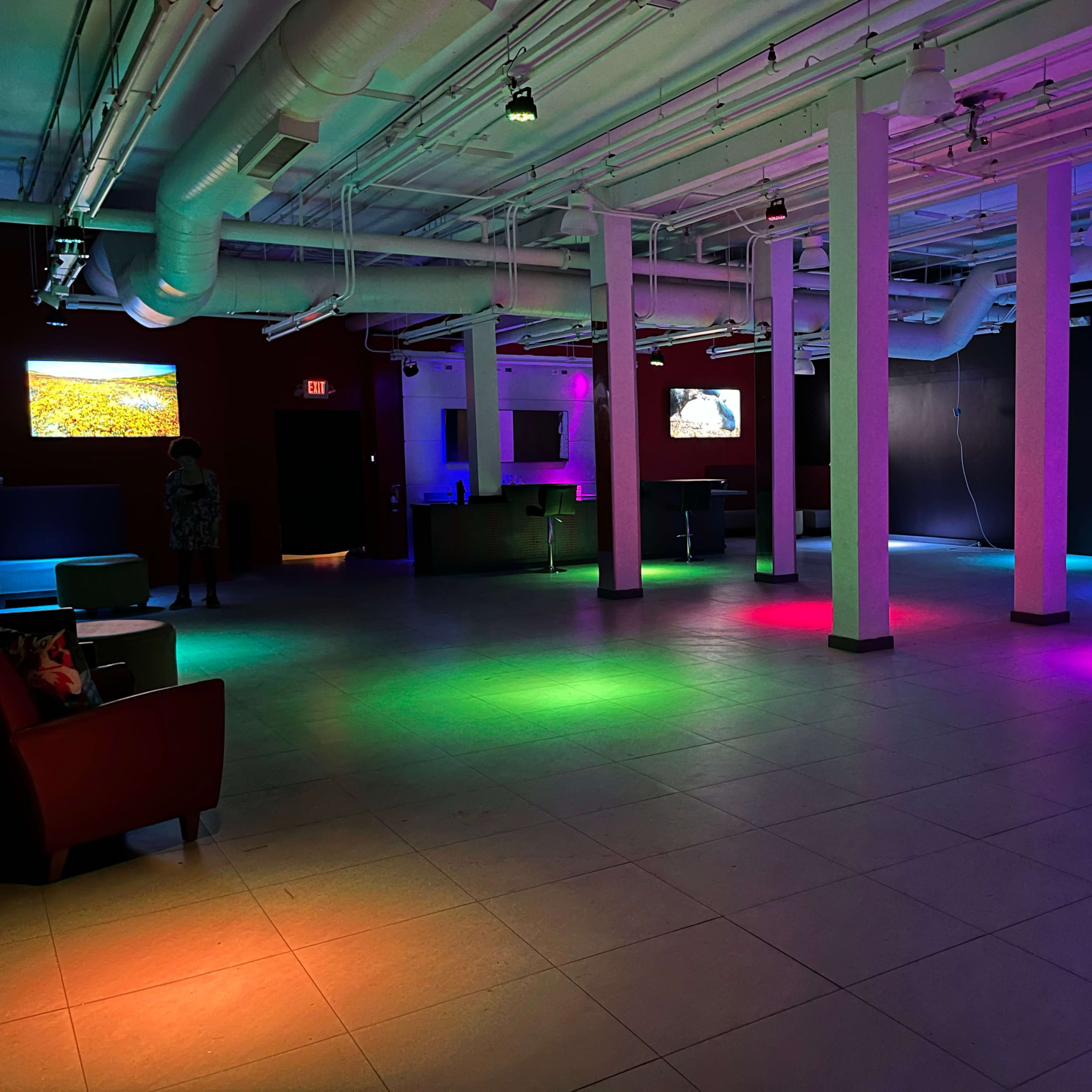 An empty room with colorful LED lights illuminating the floor and walls, along with a few screens displaying images.