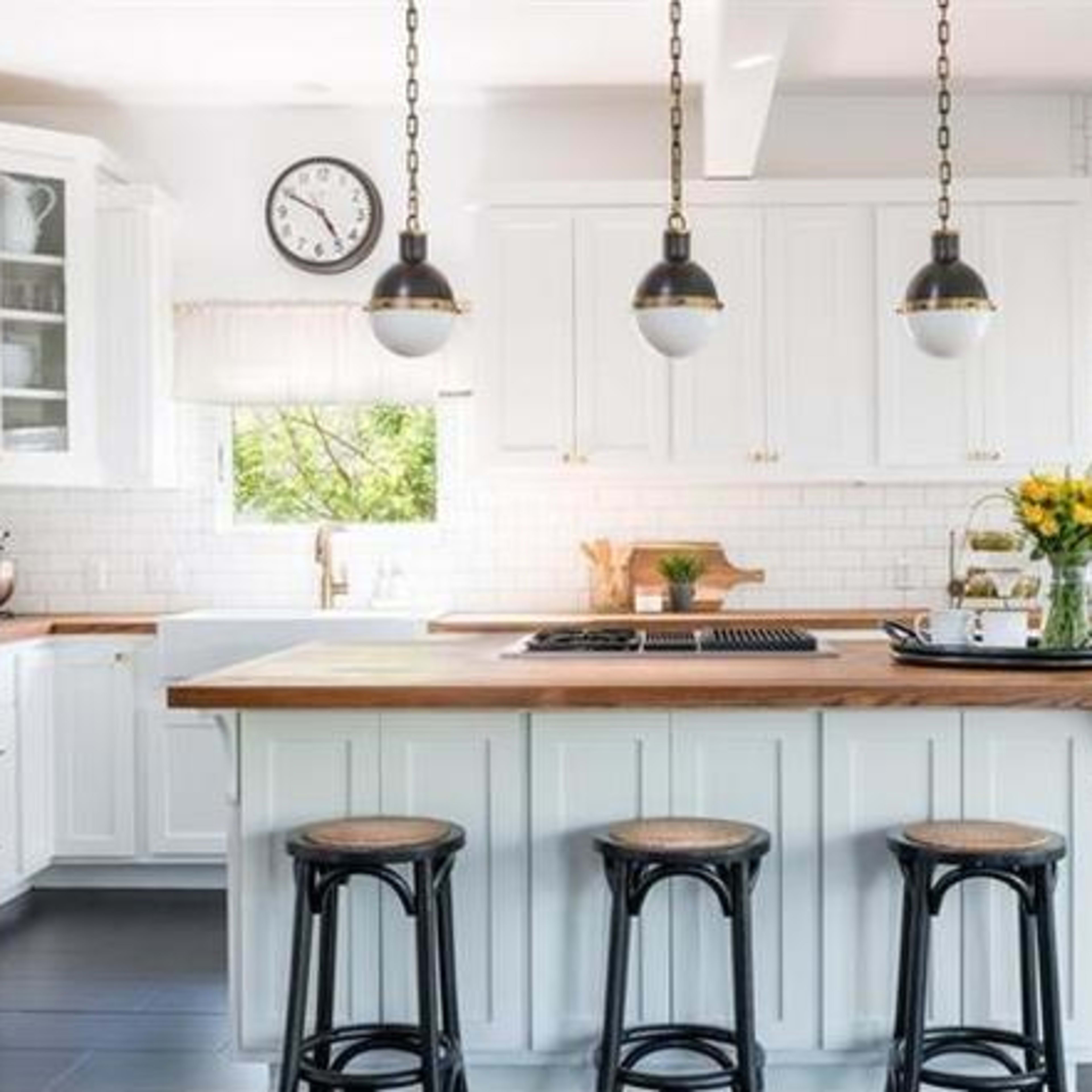 A modern kitchen features white cabinetry, a wooden island with bar stools, and pendant lights above.