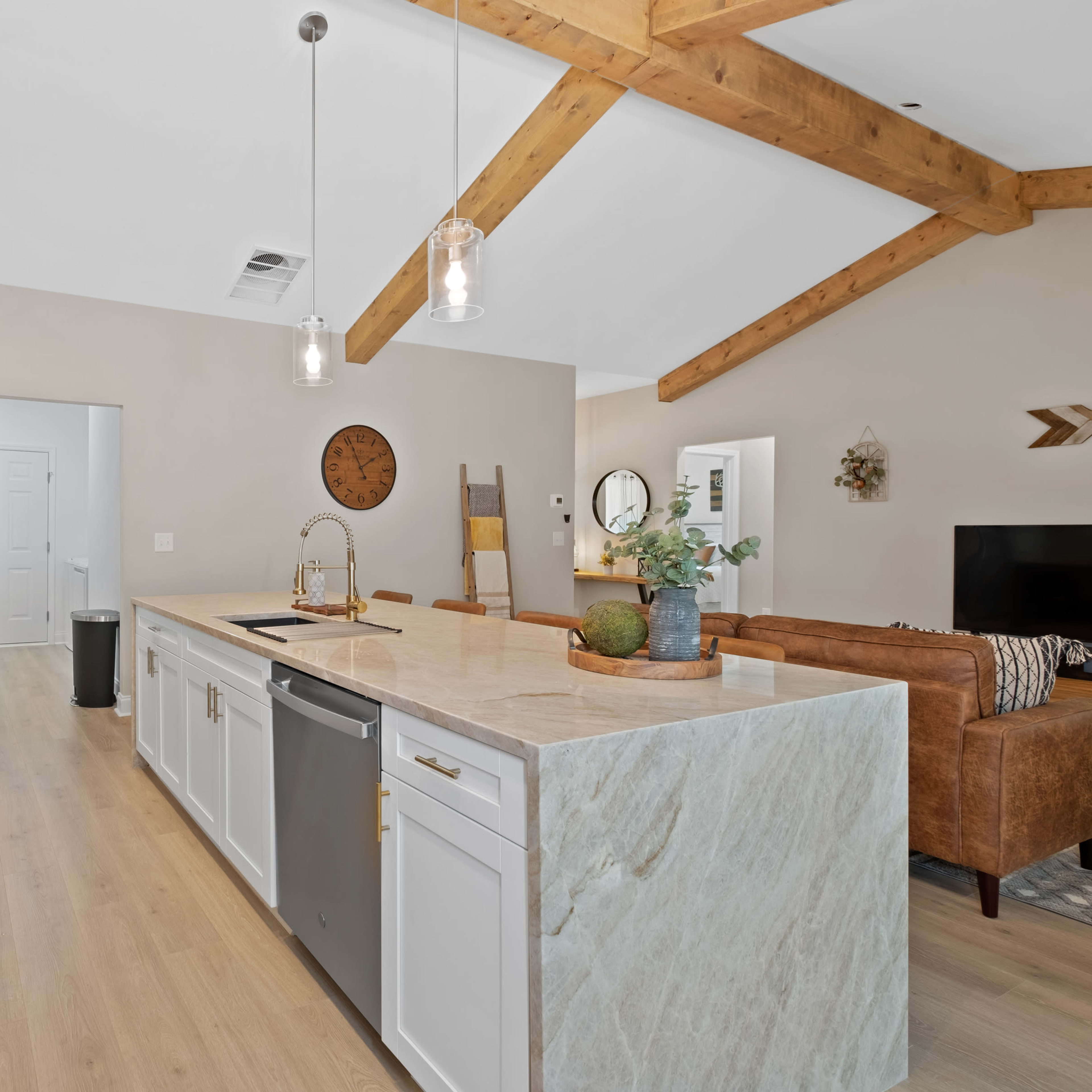 A modern kitchen with white cabinetry, a large island with a marble countertop, stainless steel appliances, and exposed wooden beams on the ceiling.