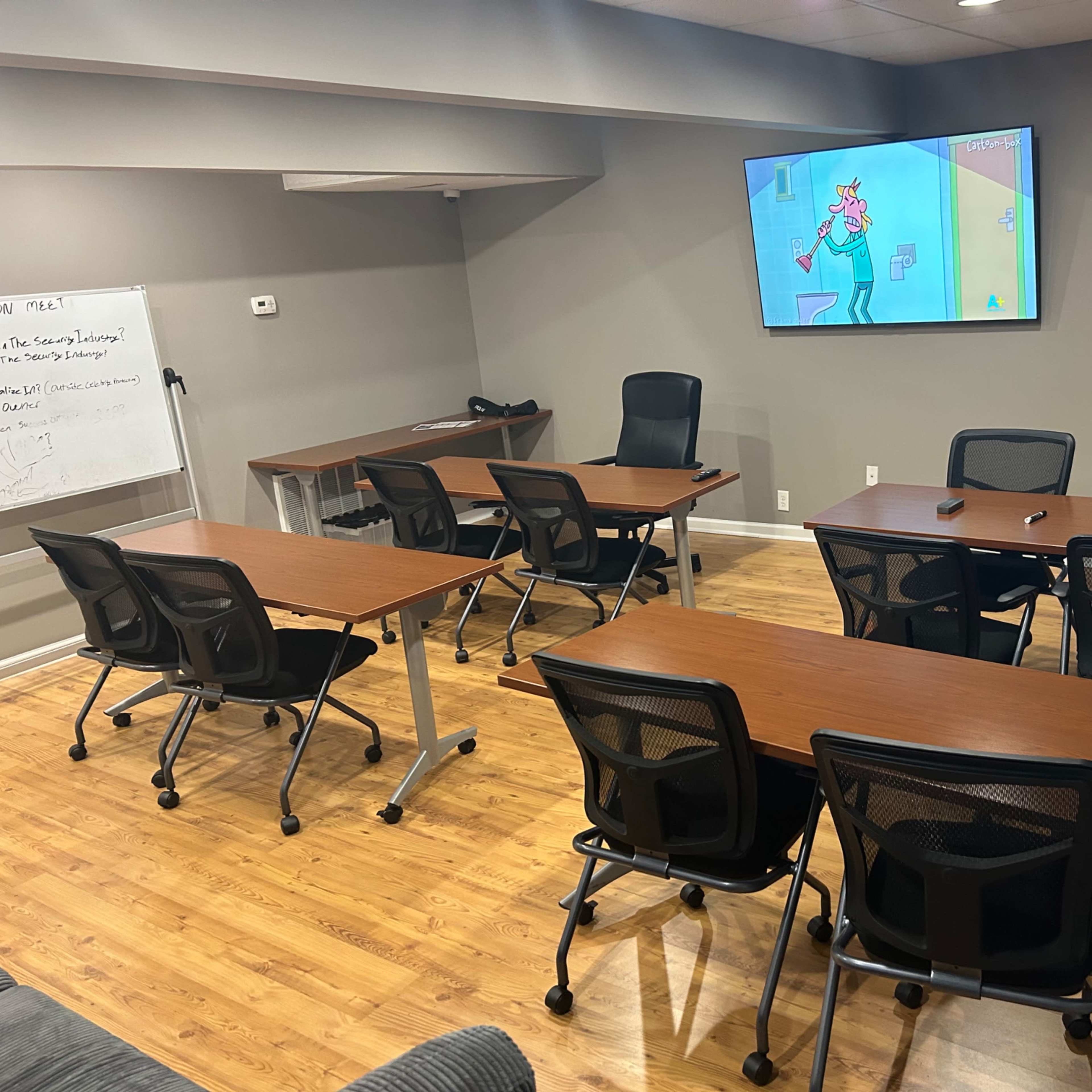A modern meeting room features several tables and chairs arranged for group collaboration, with a large screen mounted on the wall.