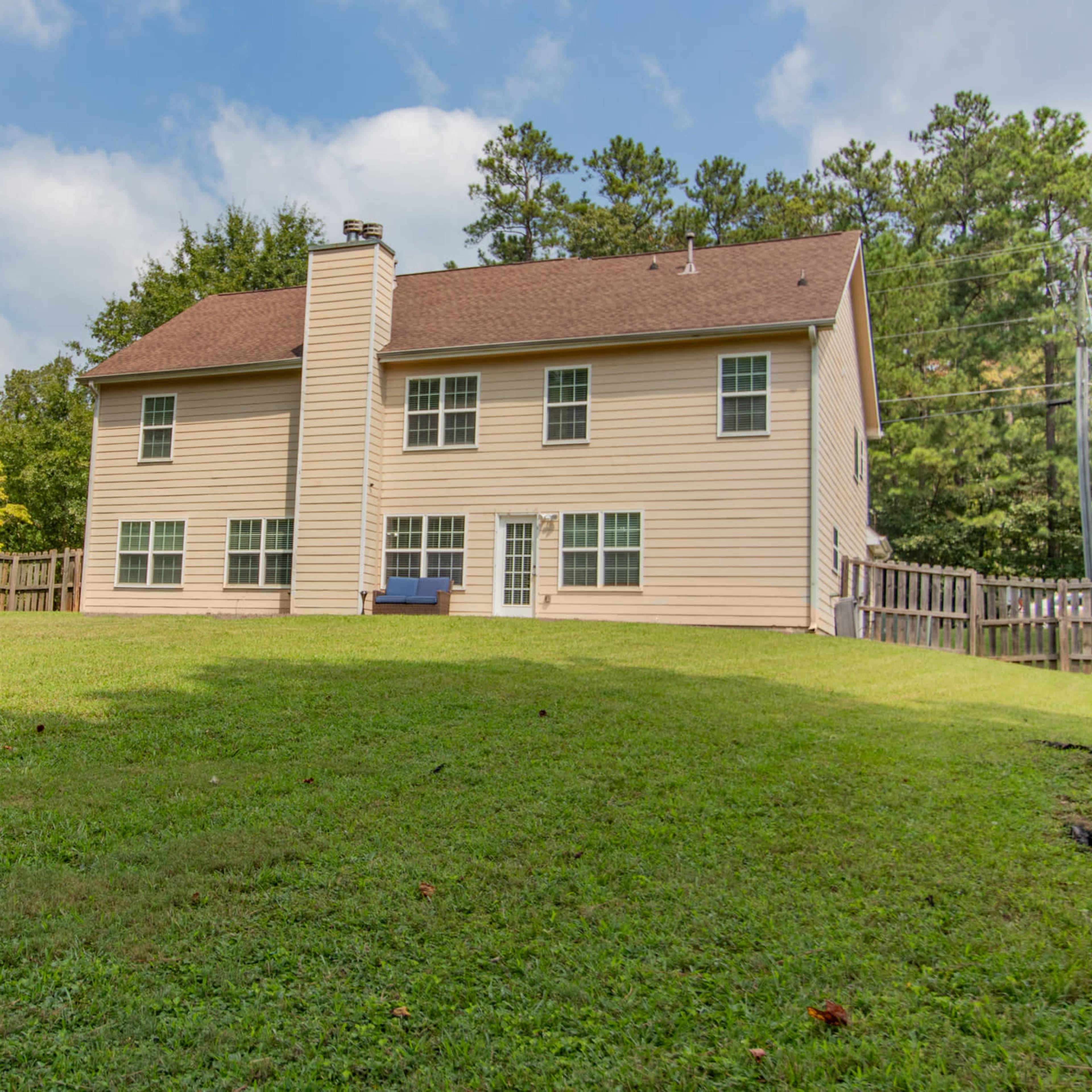 A two-story house with a fenced backyard and a flat grassy area.