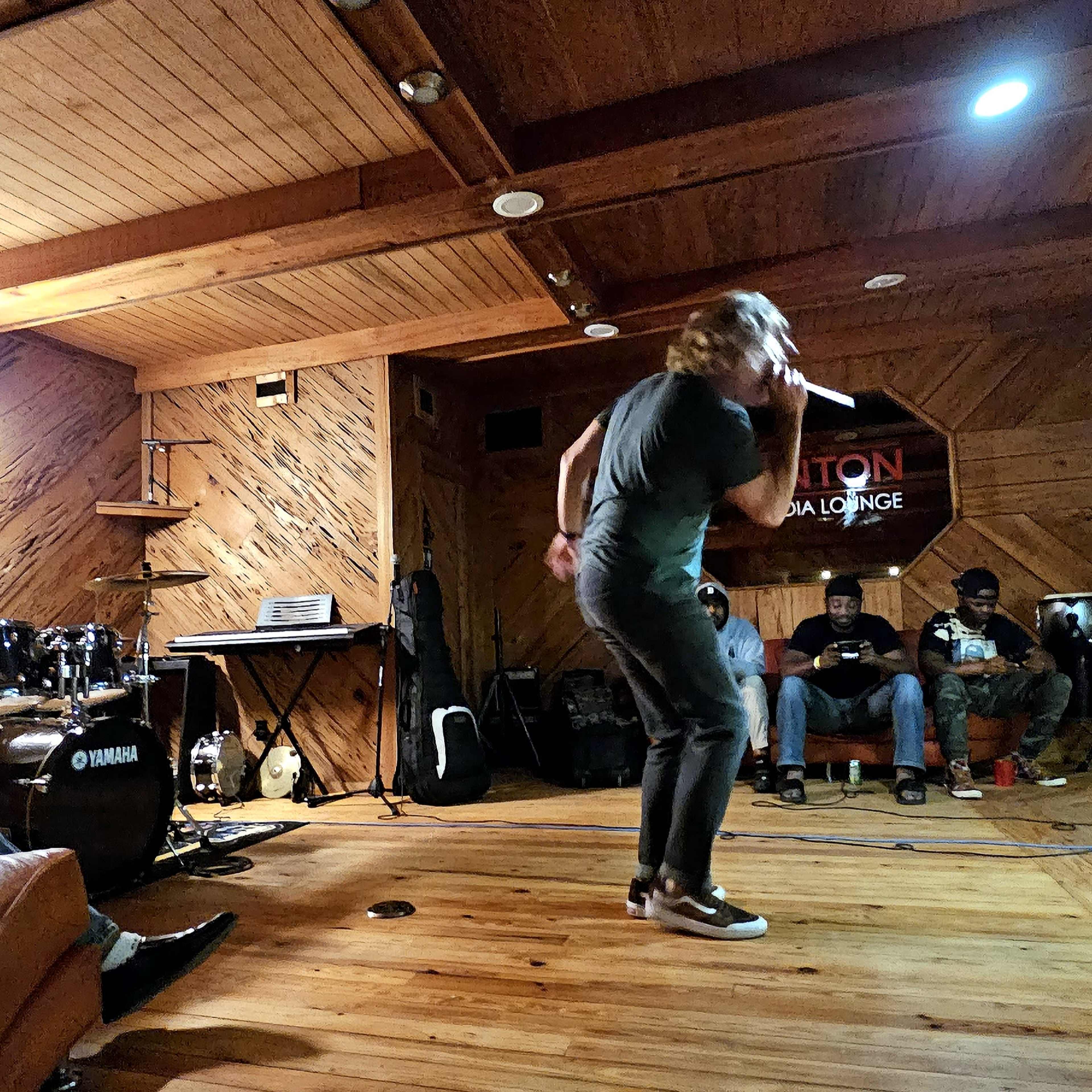 A musician performs on stage while a band plays instruments in a cozy lounge setting.