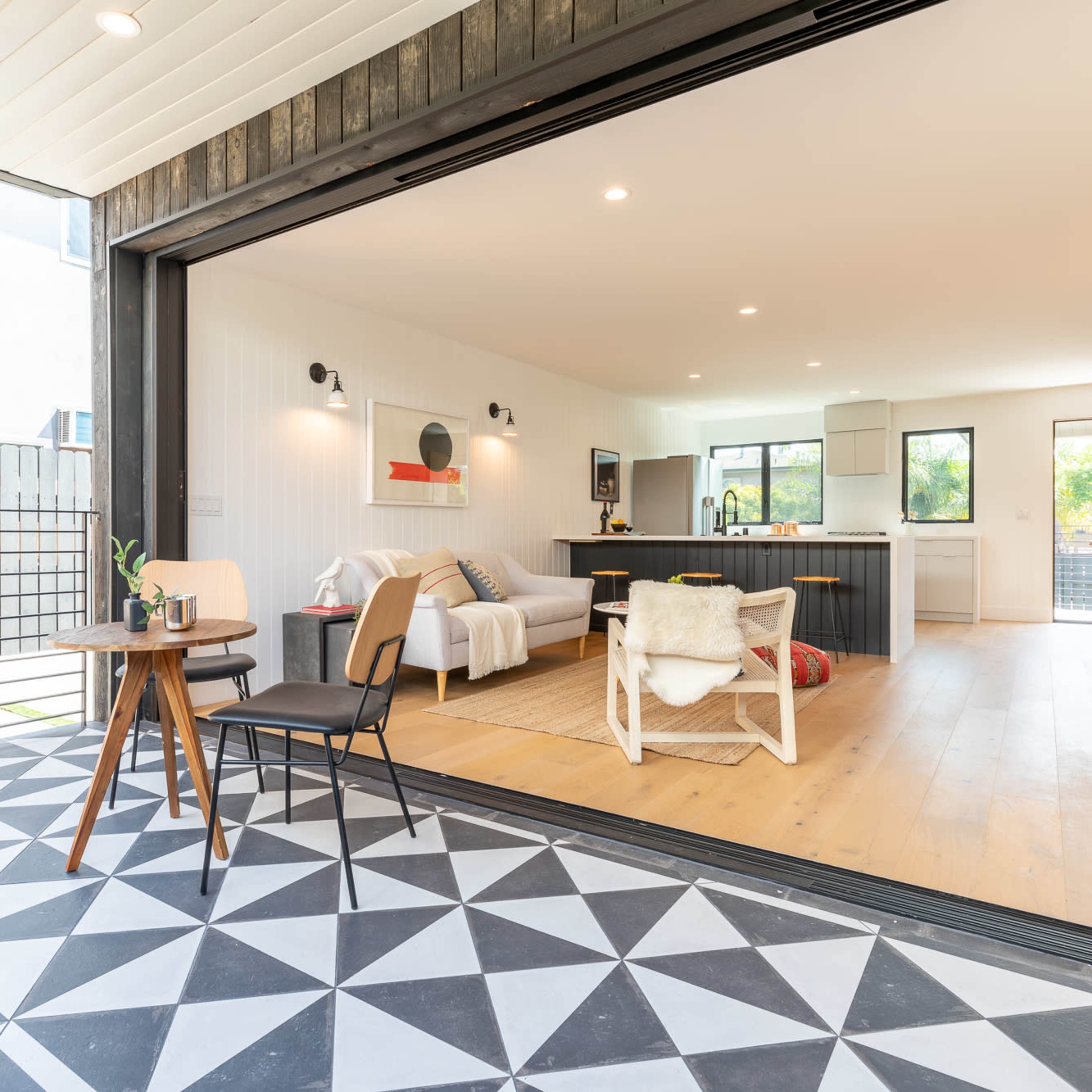 A modern living space with an open floor plan, featuring a seating area, kitchen, and a patio that opens up to a backyard.