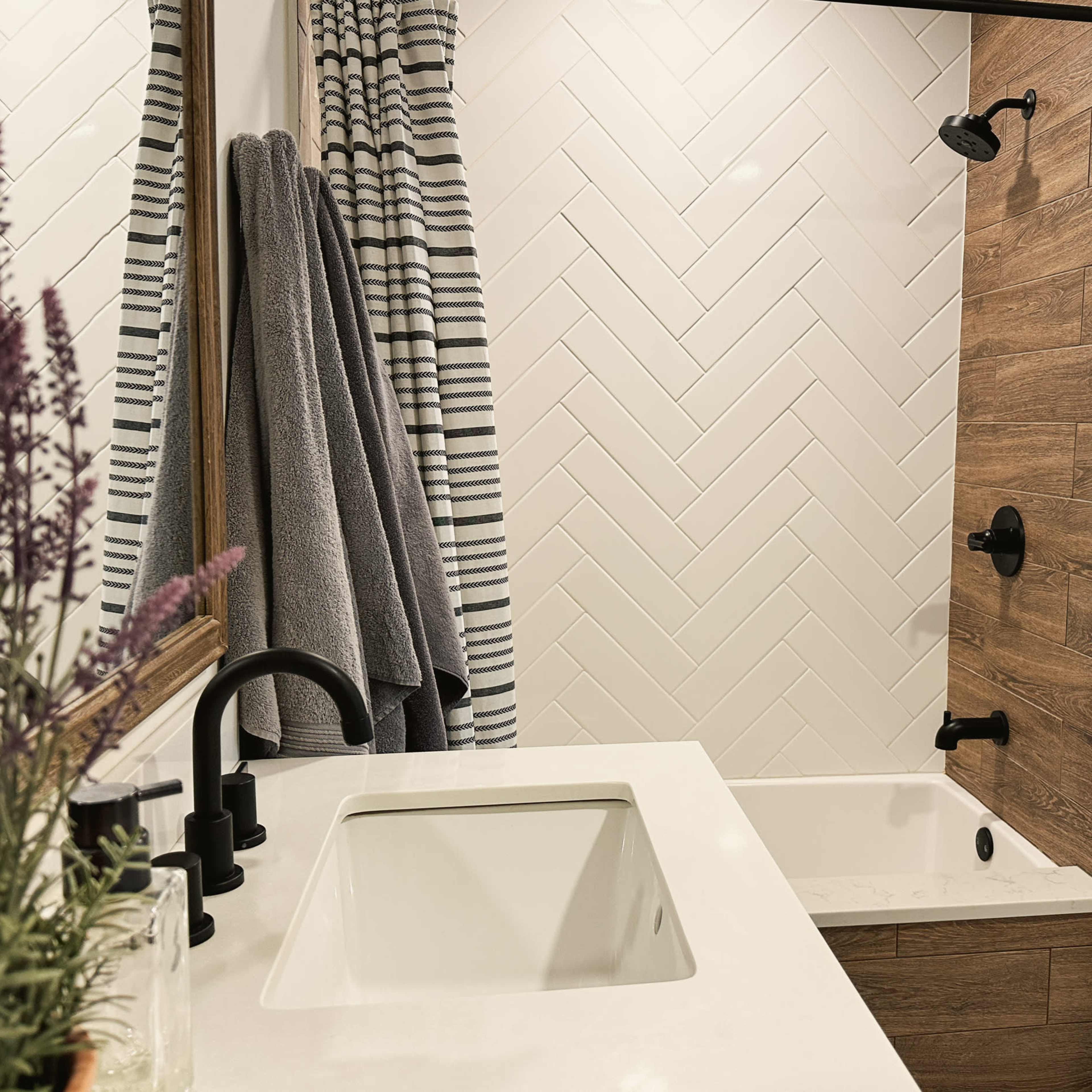 A modern bathroom featuring a bathtub with a herringbone-patterned wall, a minimalist sink, and gray tiles.
