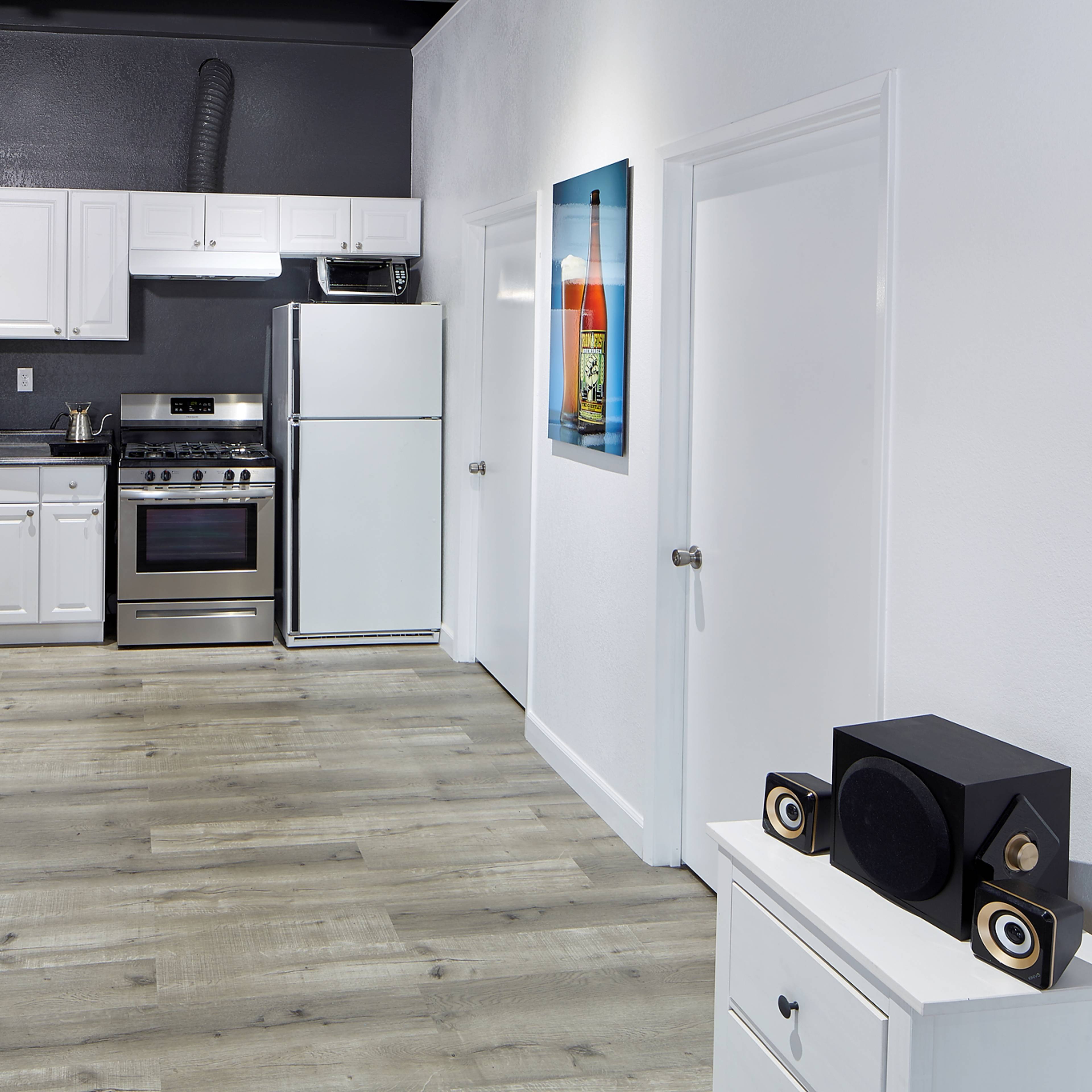 A modern kitchen with white cabinets, stainless steel appliances, and a light-colored wooden floor.