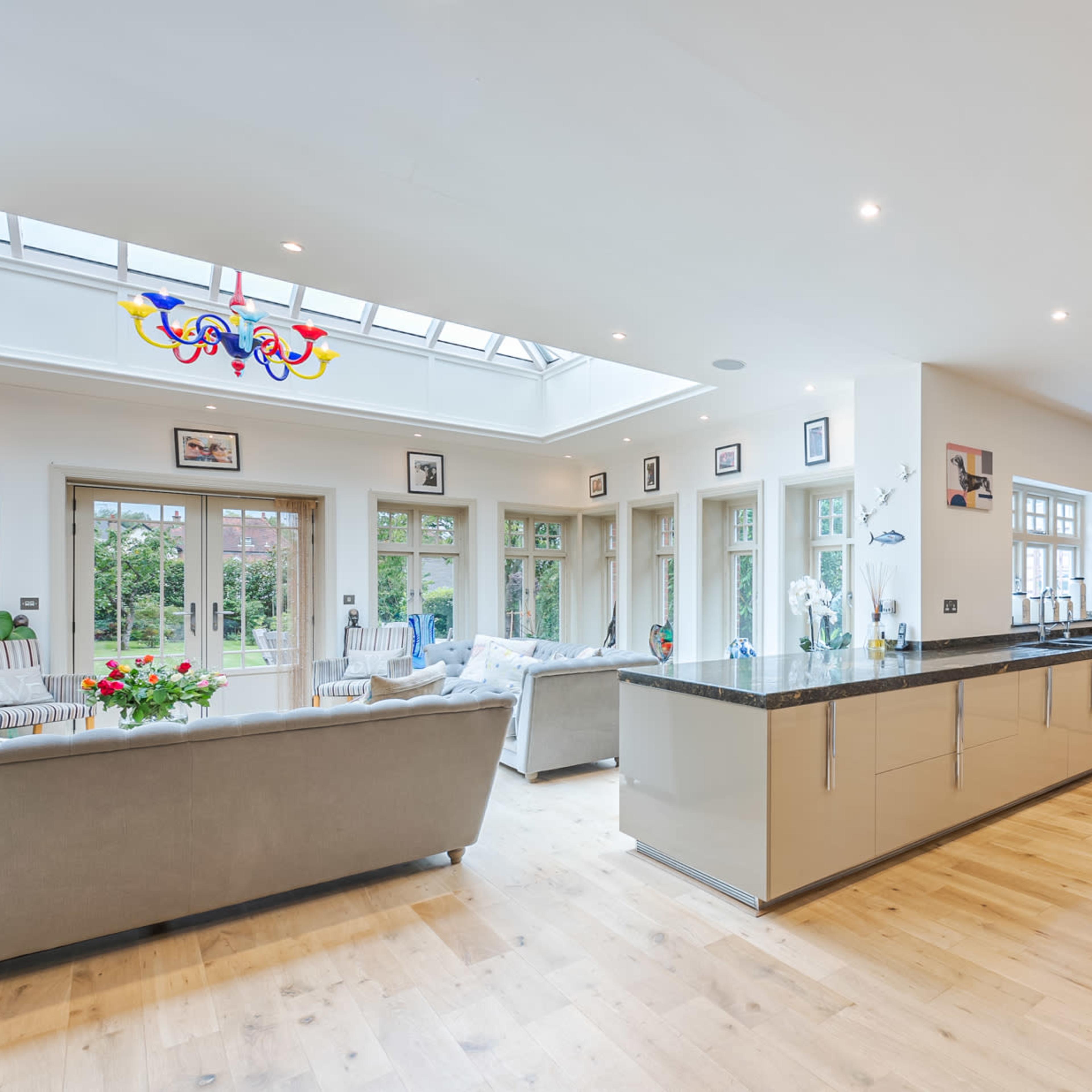 A modern kitchen features a large central island, sleek cabinetry, and an open layout that leads to a bright living area with large windows.