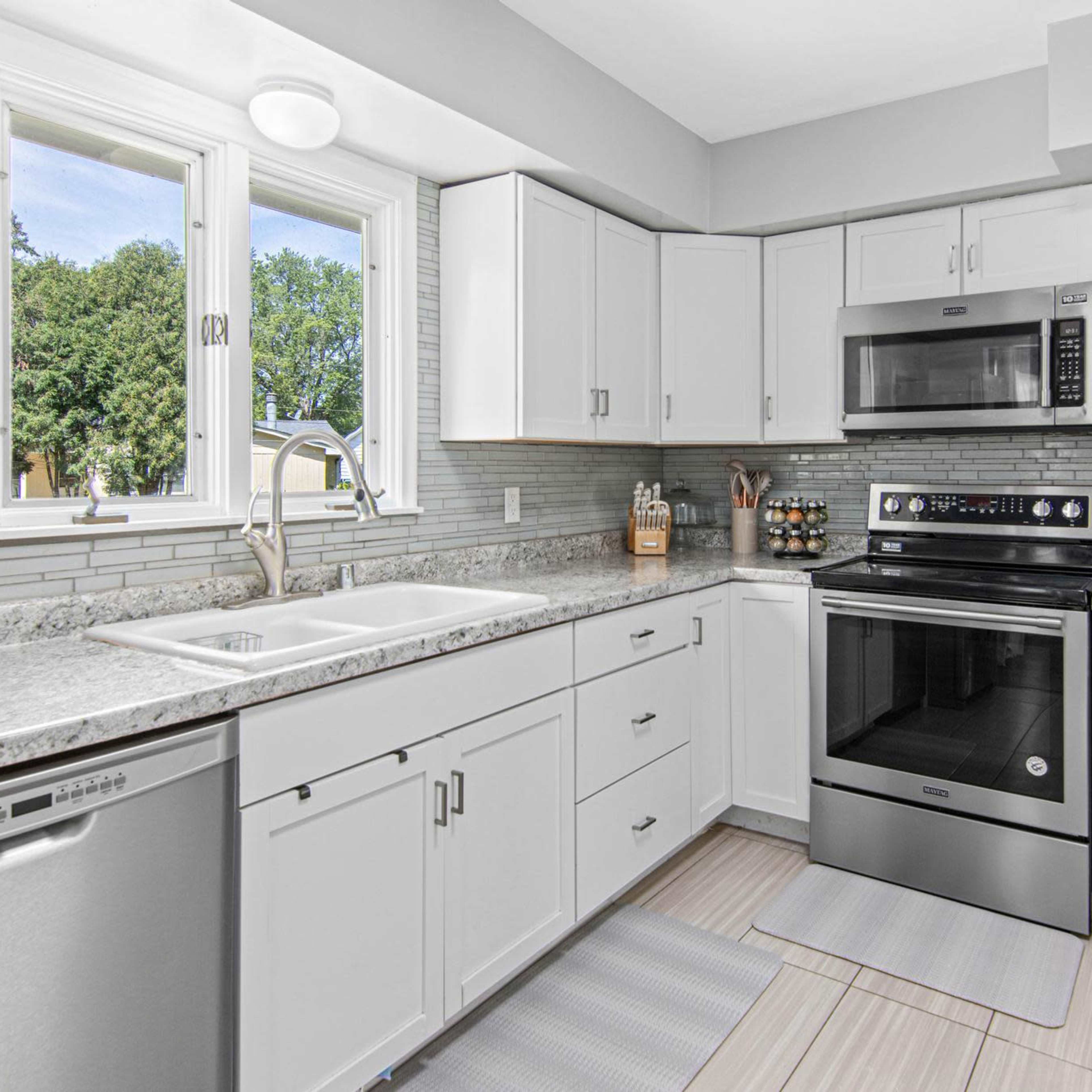 A modern kitchen features white cabinetry, stainless steel appliances, and granite countertops with a window providing natural light.