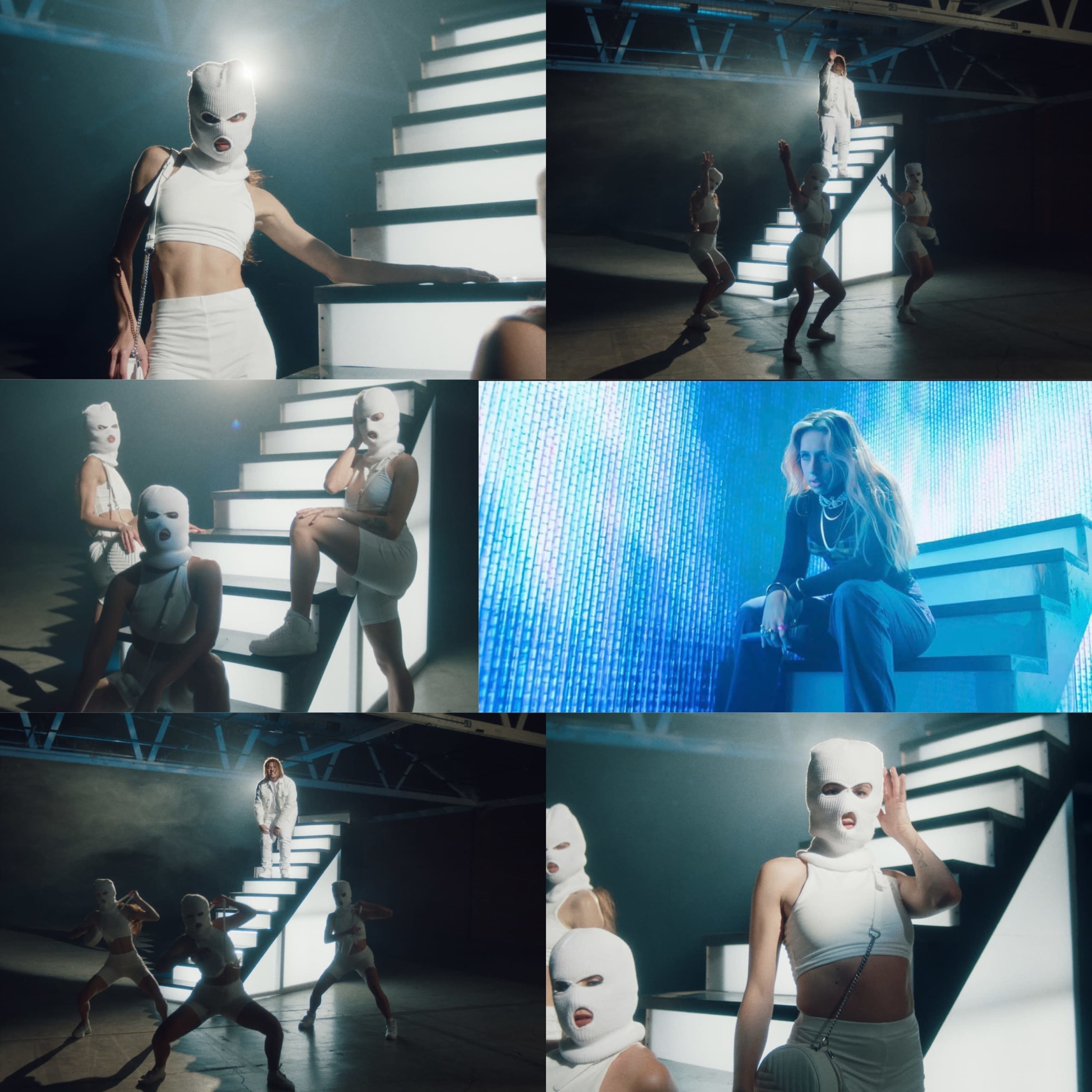A group of performers wearing white masks, posing in various configurations around illuminated steps in a dimly lit space.
