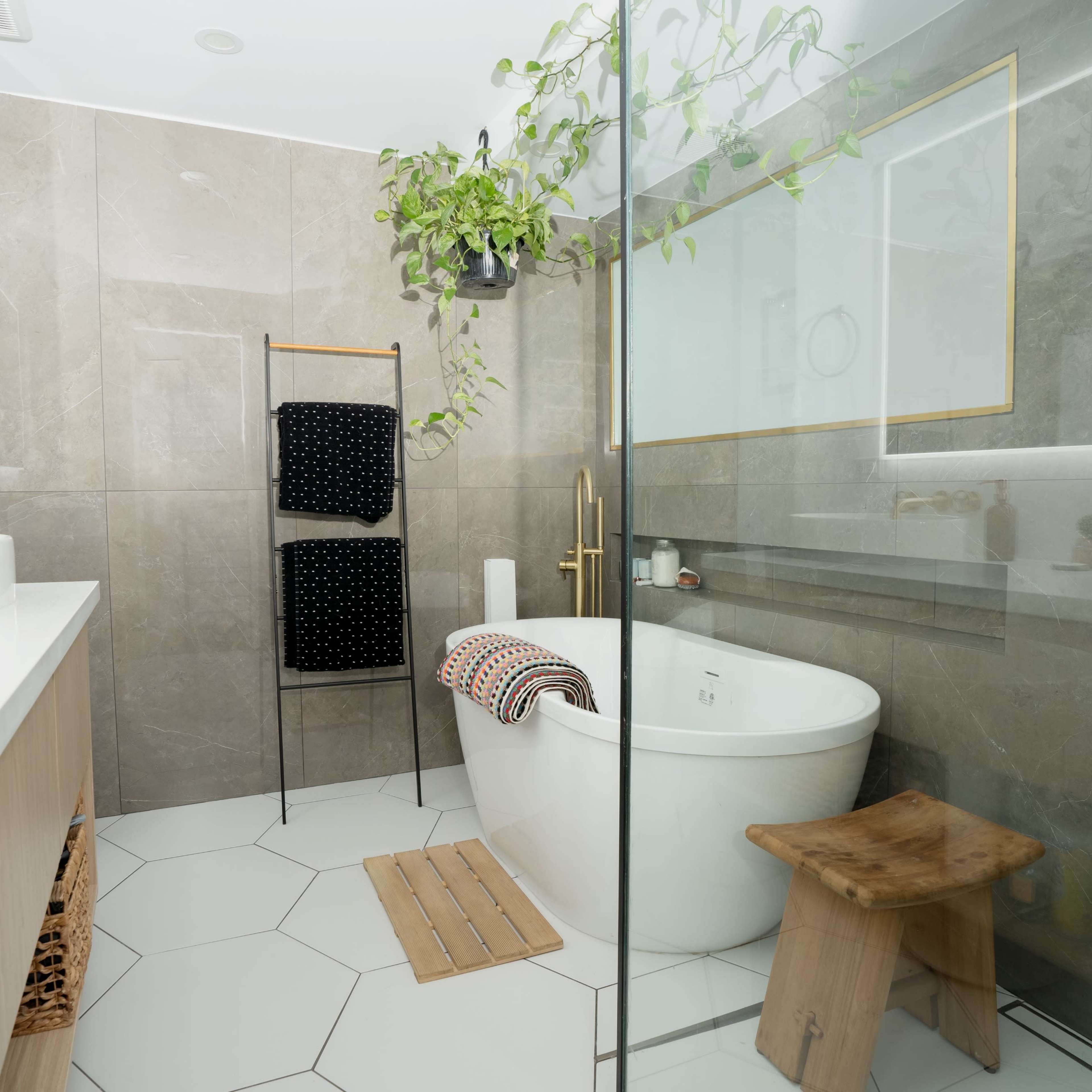 A modern bathroom featuring a freestanding bathtub, a glass shower, a wooden stool, and plants hanging from the ceiling.