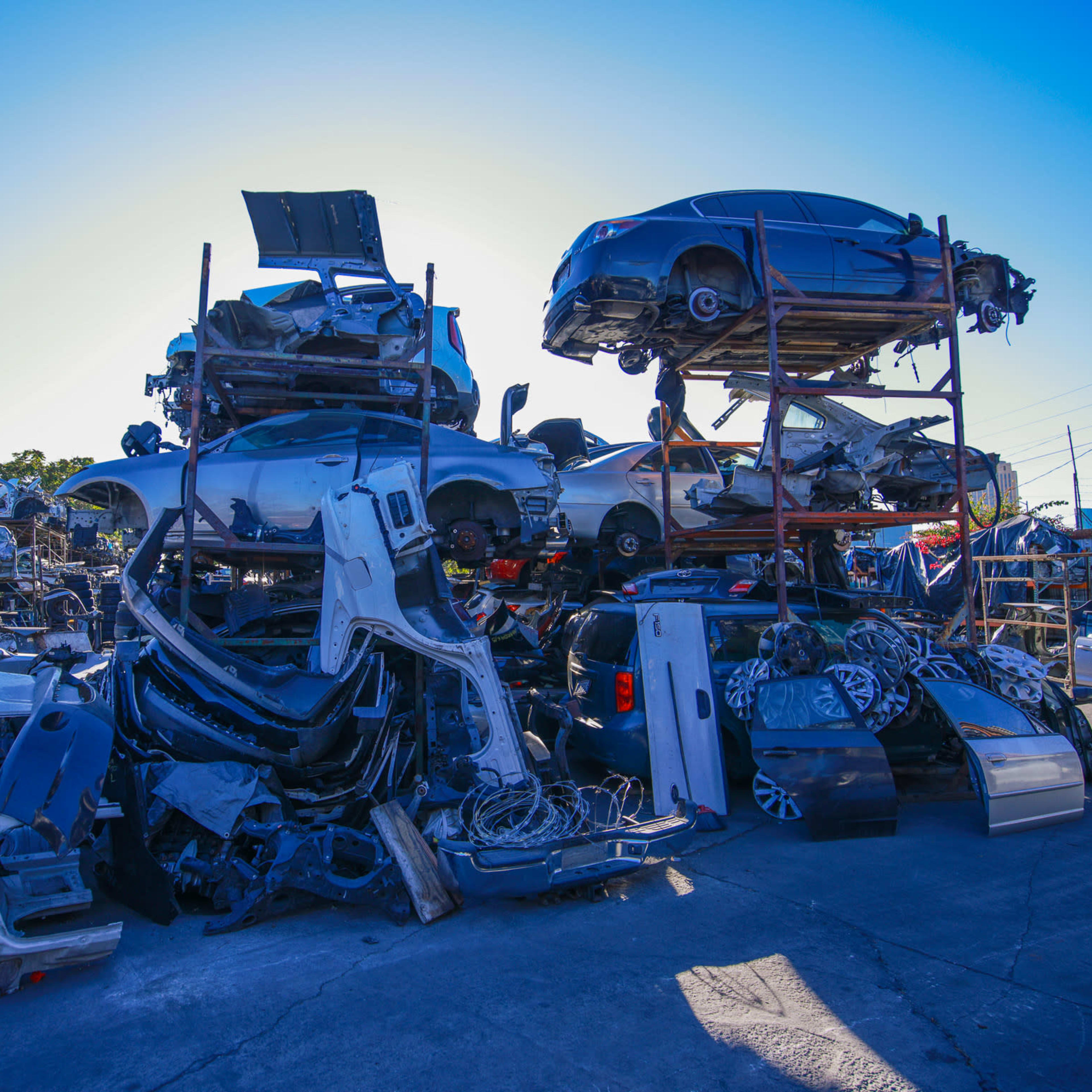 A junkyard filled with stacked cars and vehicle parts under a clear blue sky.