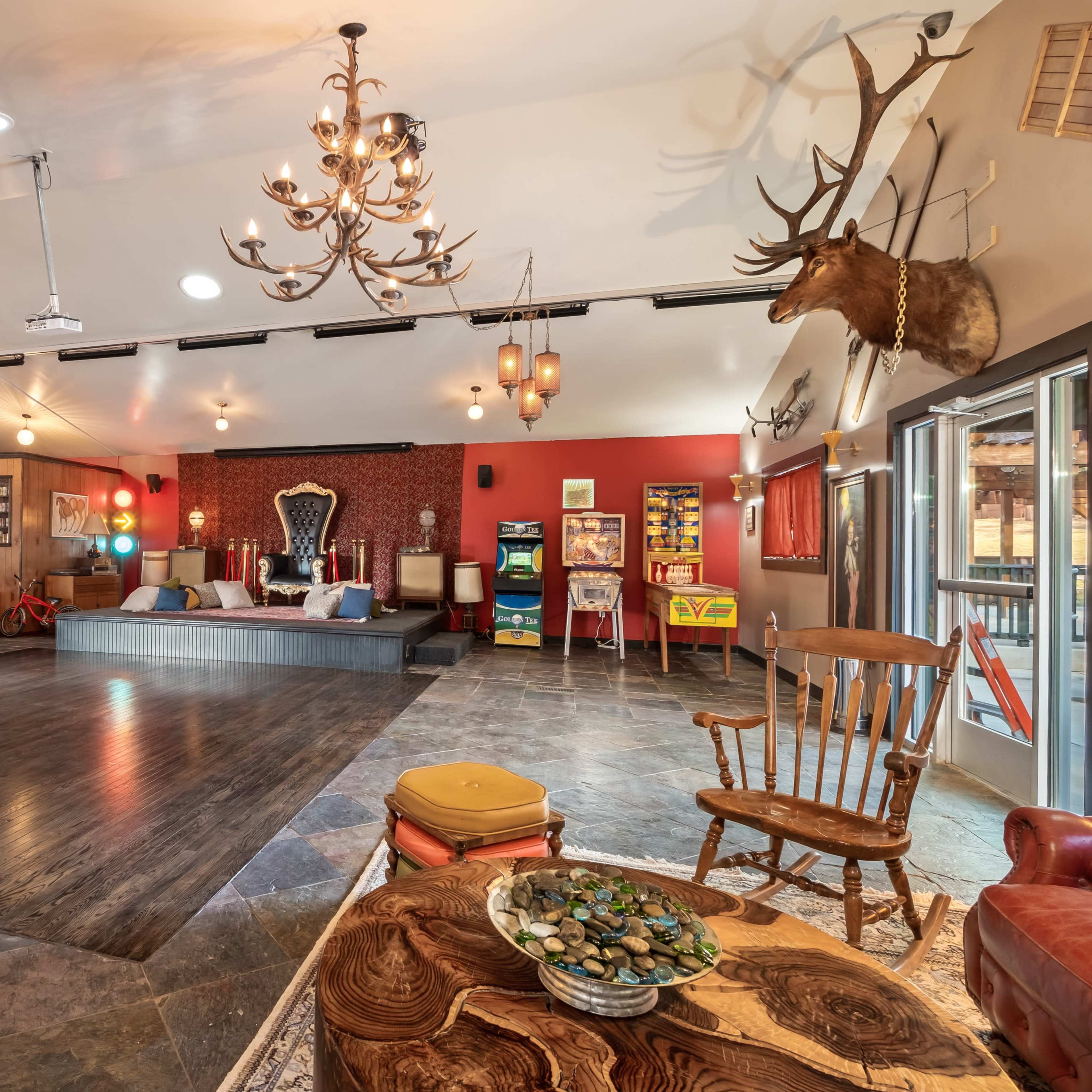A spacious interior featuring a combination of seating, decorative chandeliers, and rustic decor, including mounted animal heads and vintage arcade games.