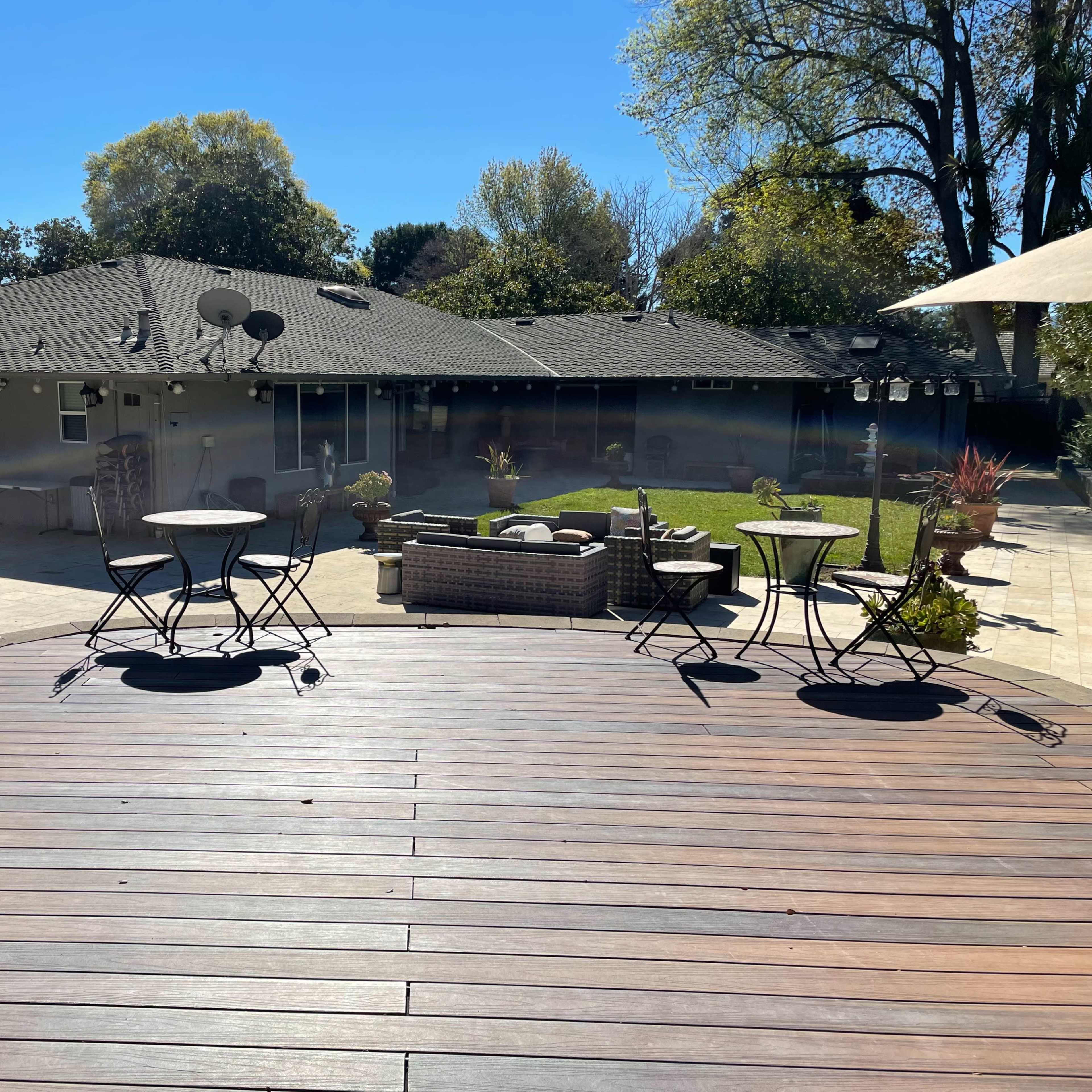 A spacious backyard with a patio, seating areas, and a lawn, surrounded by trees and a house in the background.