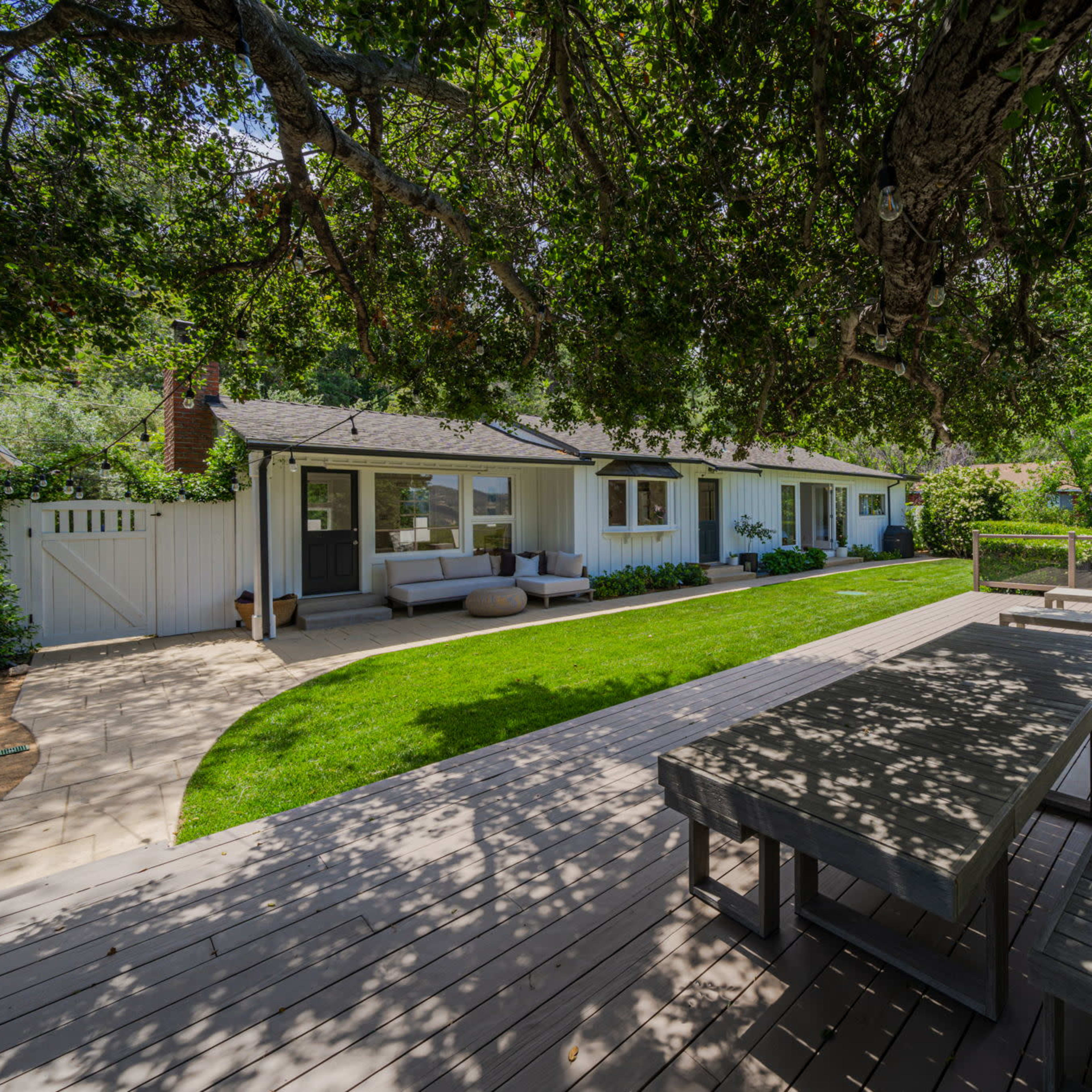 A modern house with a large wooden deck and a spacious lawn surrounded by trees.