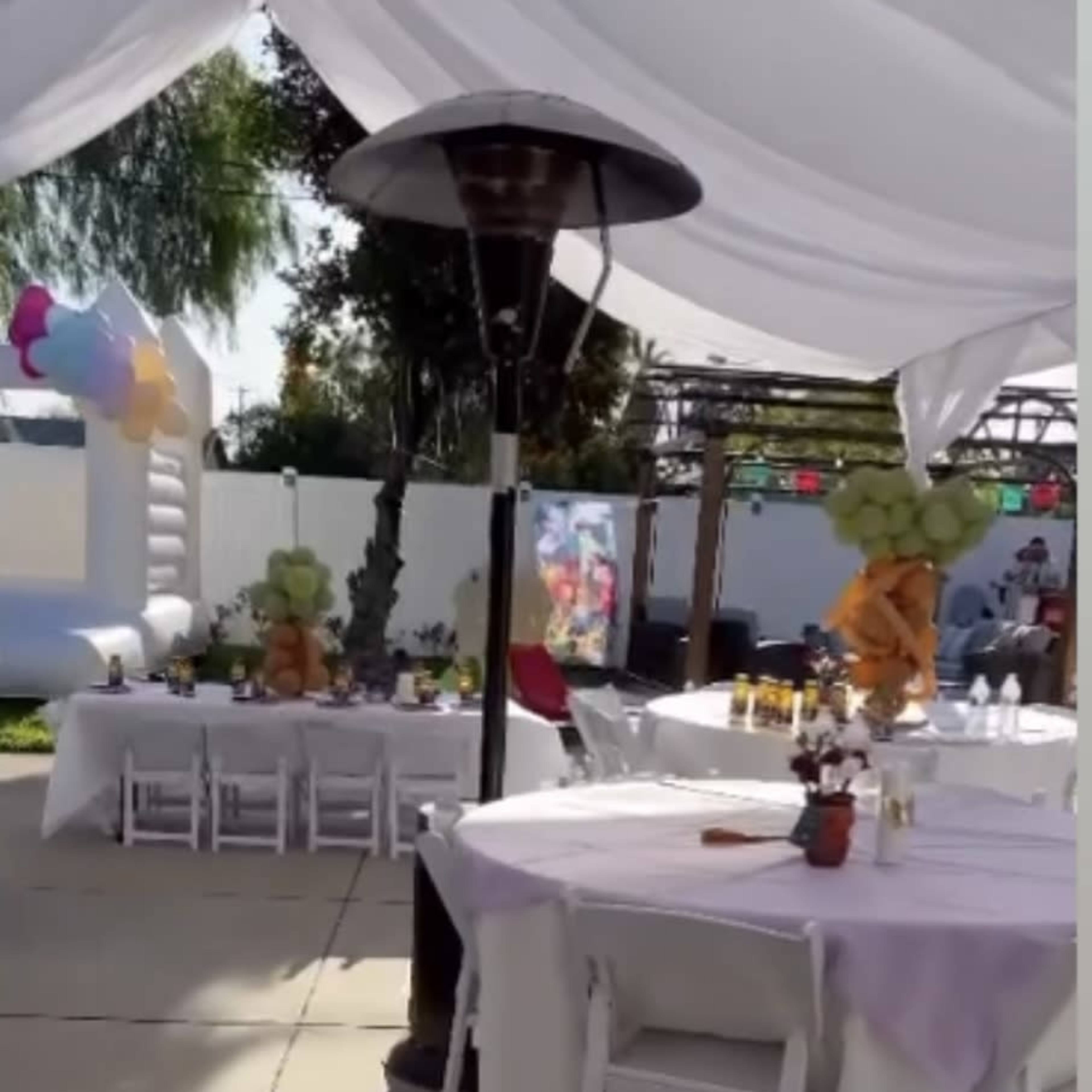 A spacious outdoor area is set up for a gathering, featuring tables covered with light purple cloths and a nearby inflatable structure.