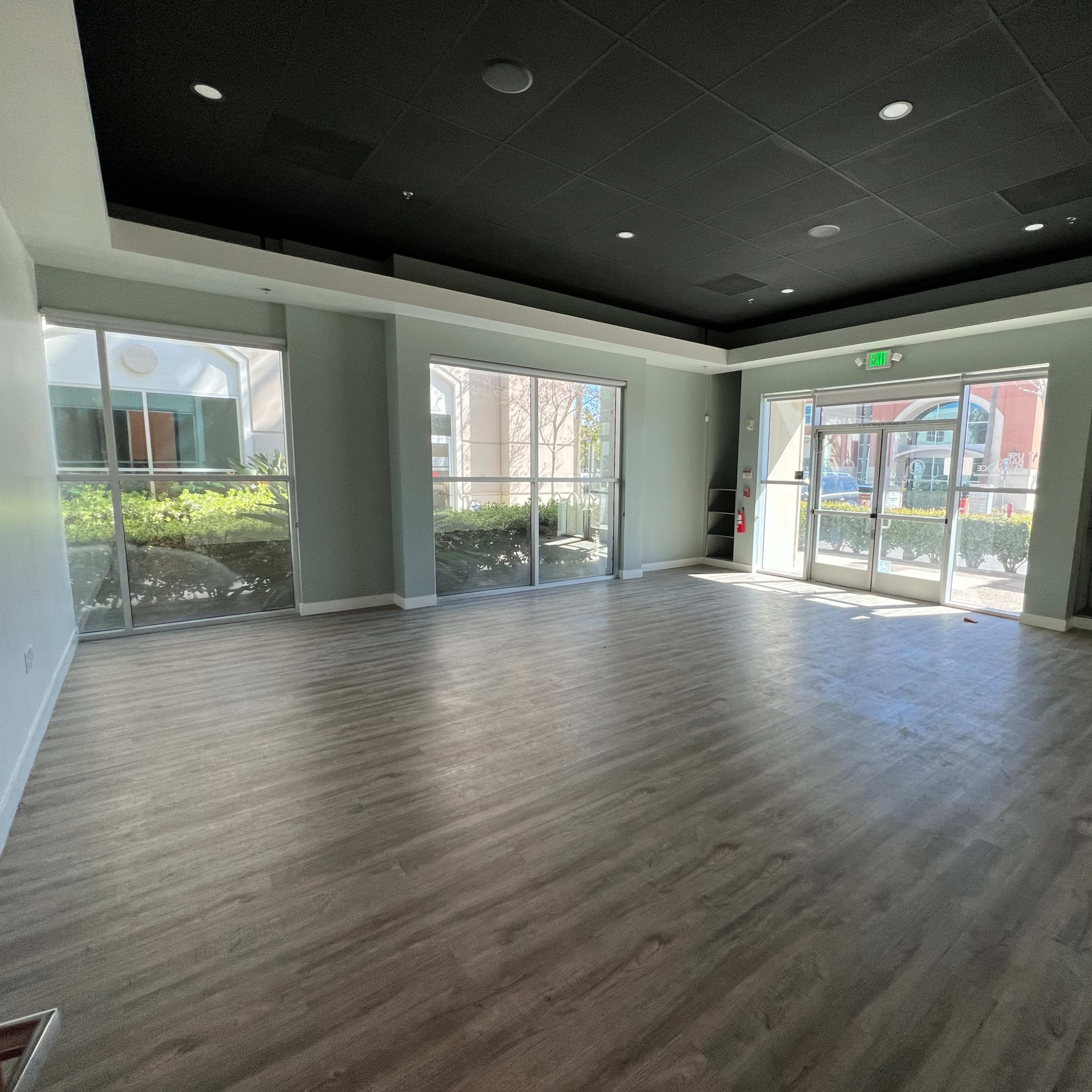 A spacious, empty room with large windows and a door leading to an outdoor area.