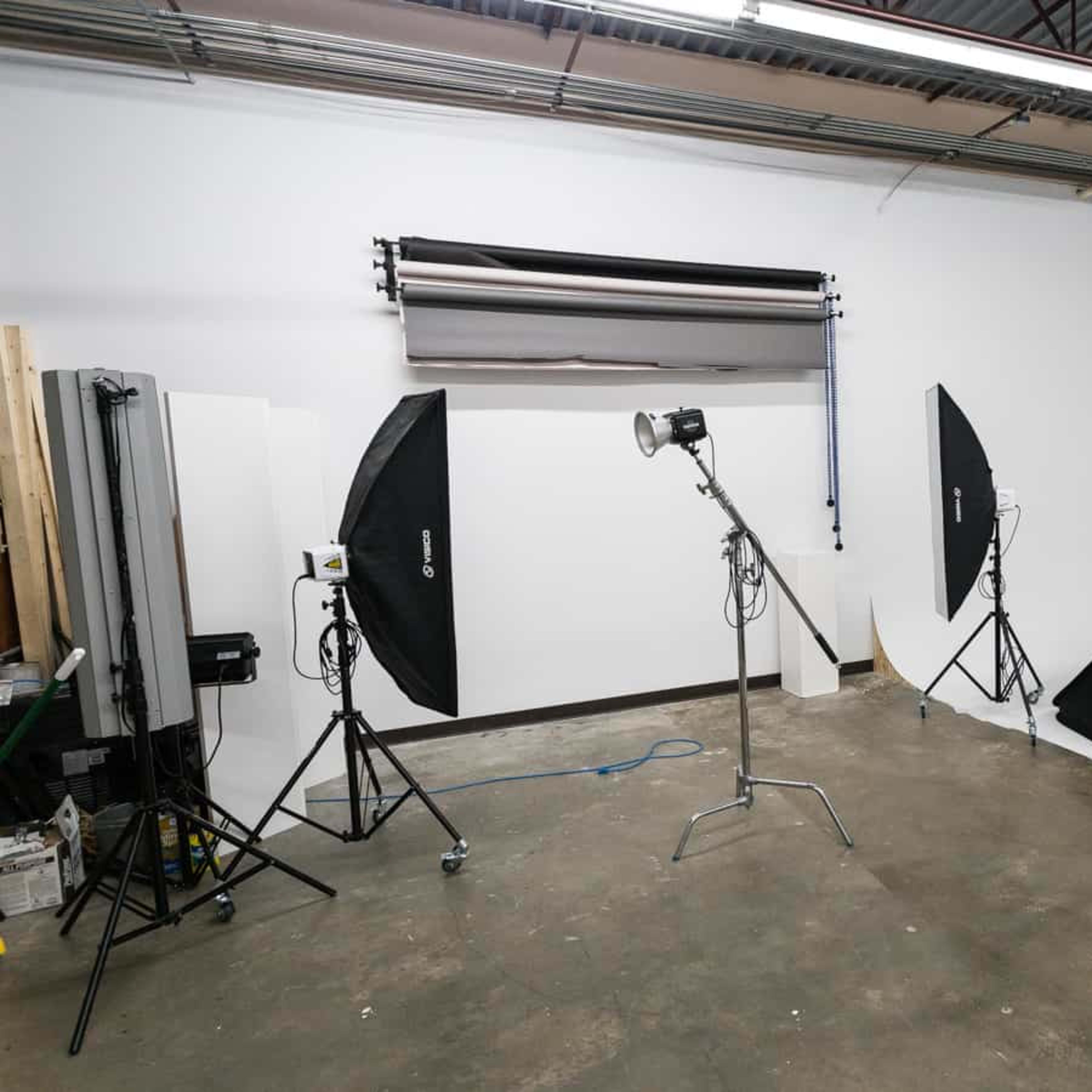 A photography studio is set up with various lighting equipment and backdrops against a white wall.