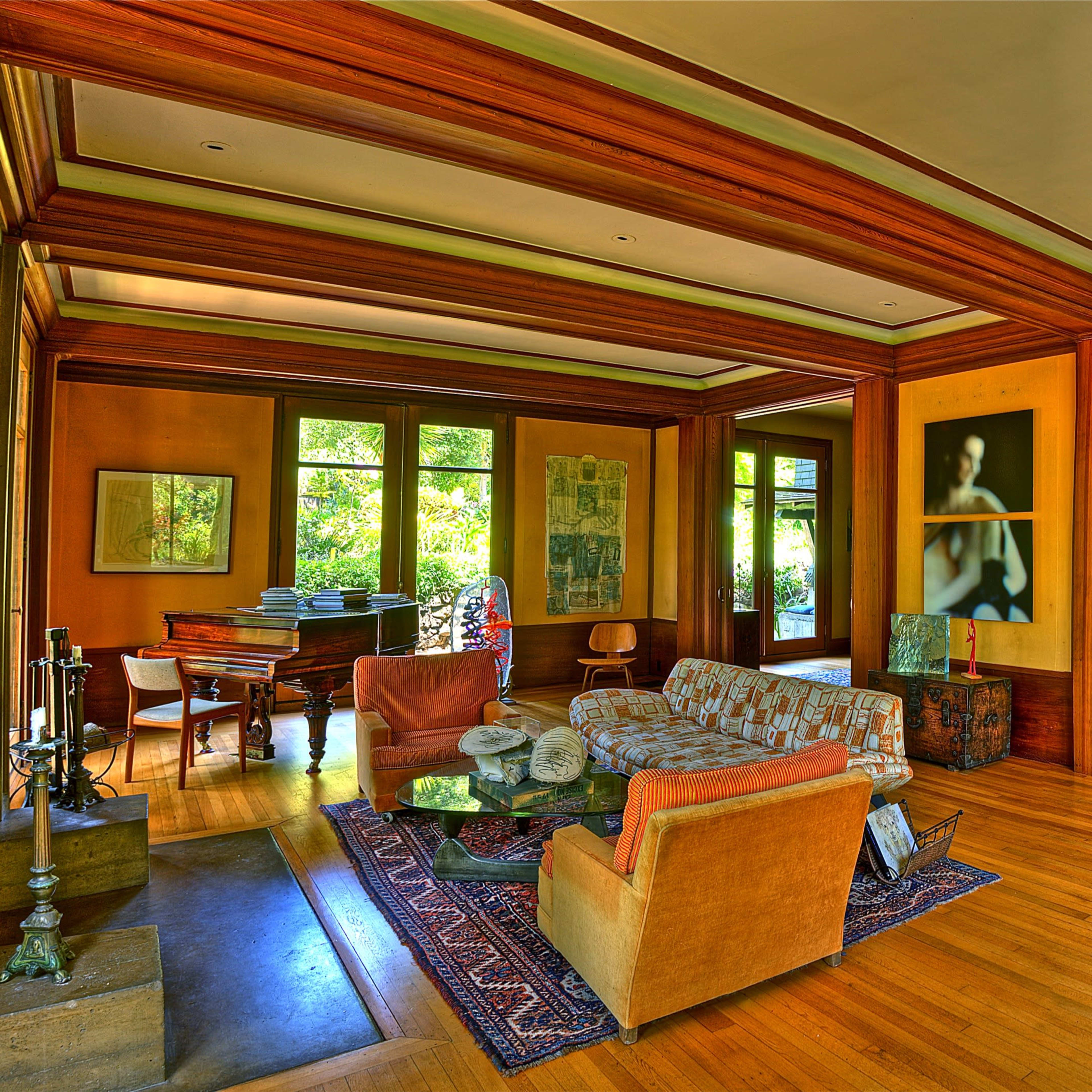 A spacious interior of a house featuring a living area with wooden beams, a piano, and various artworks on the walls.