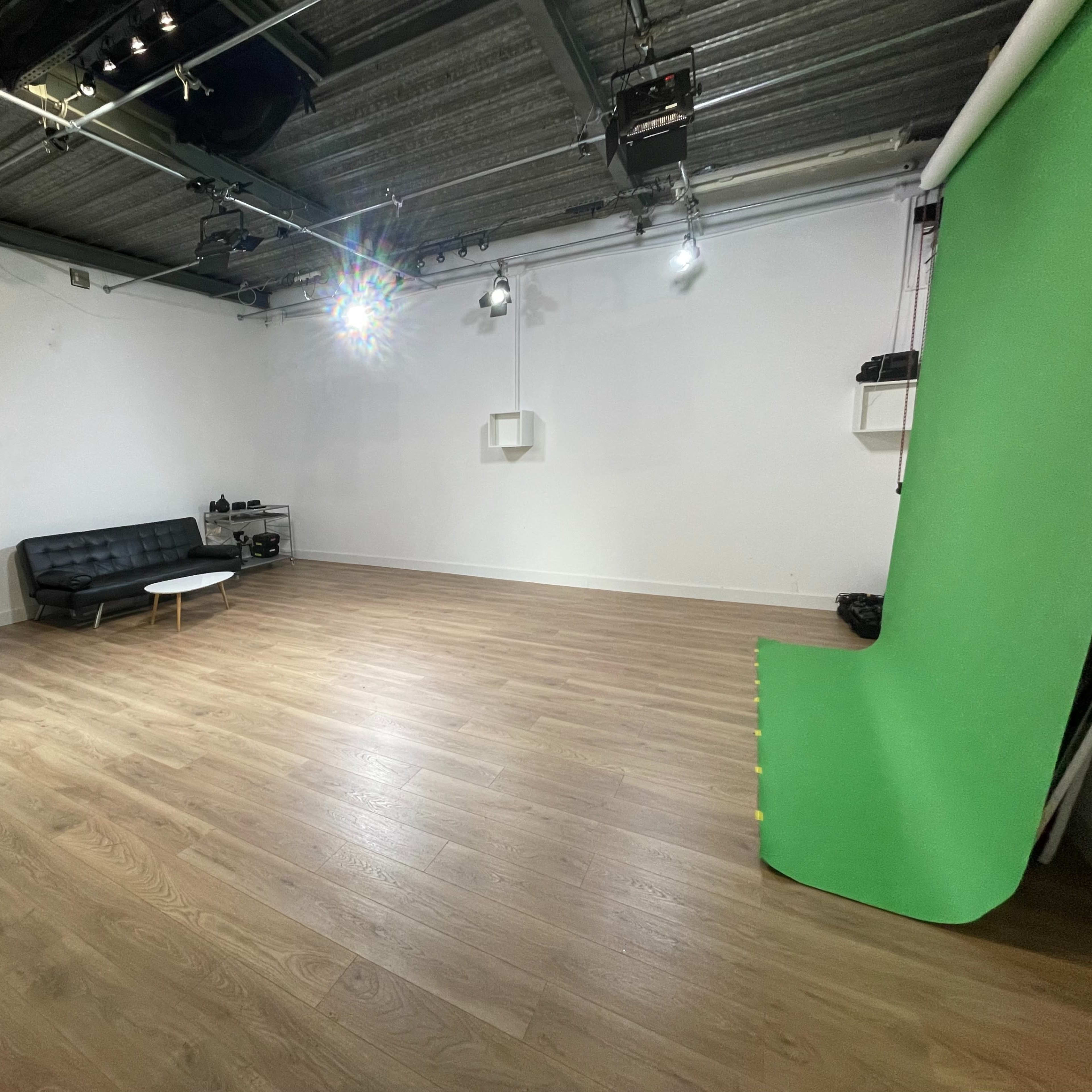 An empty photo studio featuring a black sofa, a small white coffee table, and a green backdrop along one wall.