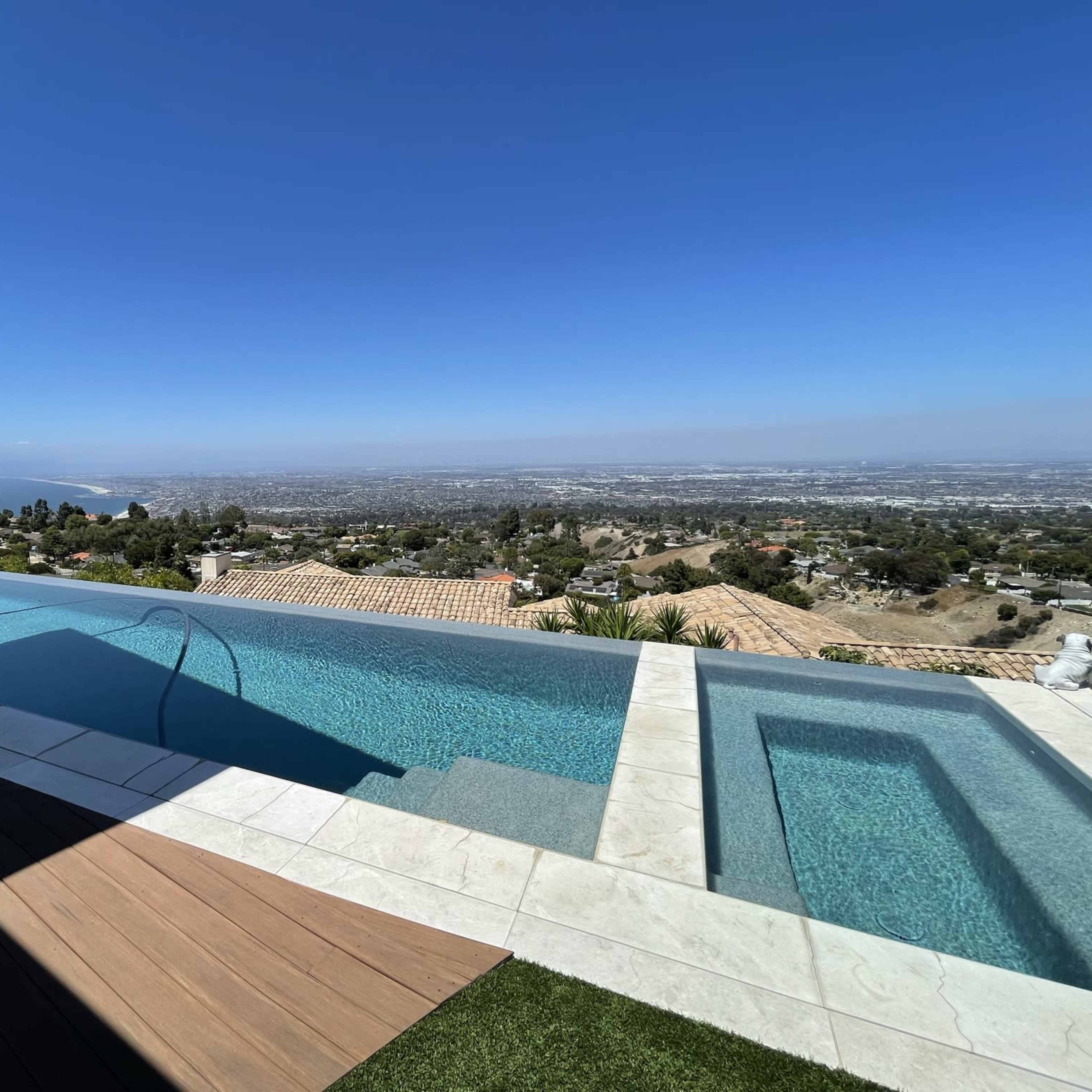 A modern infinity pool overlooking a sprawling urban landscape and distant coastline.