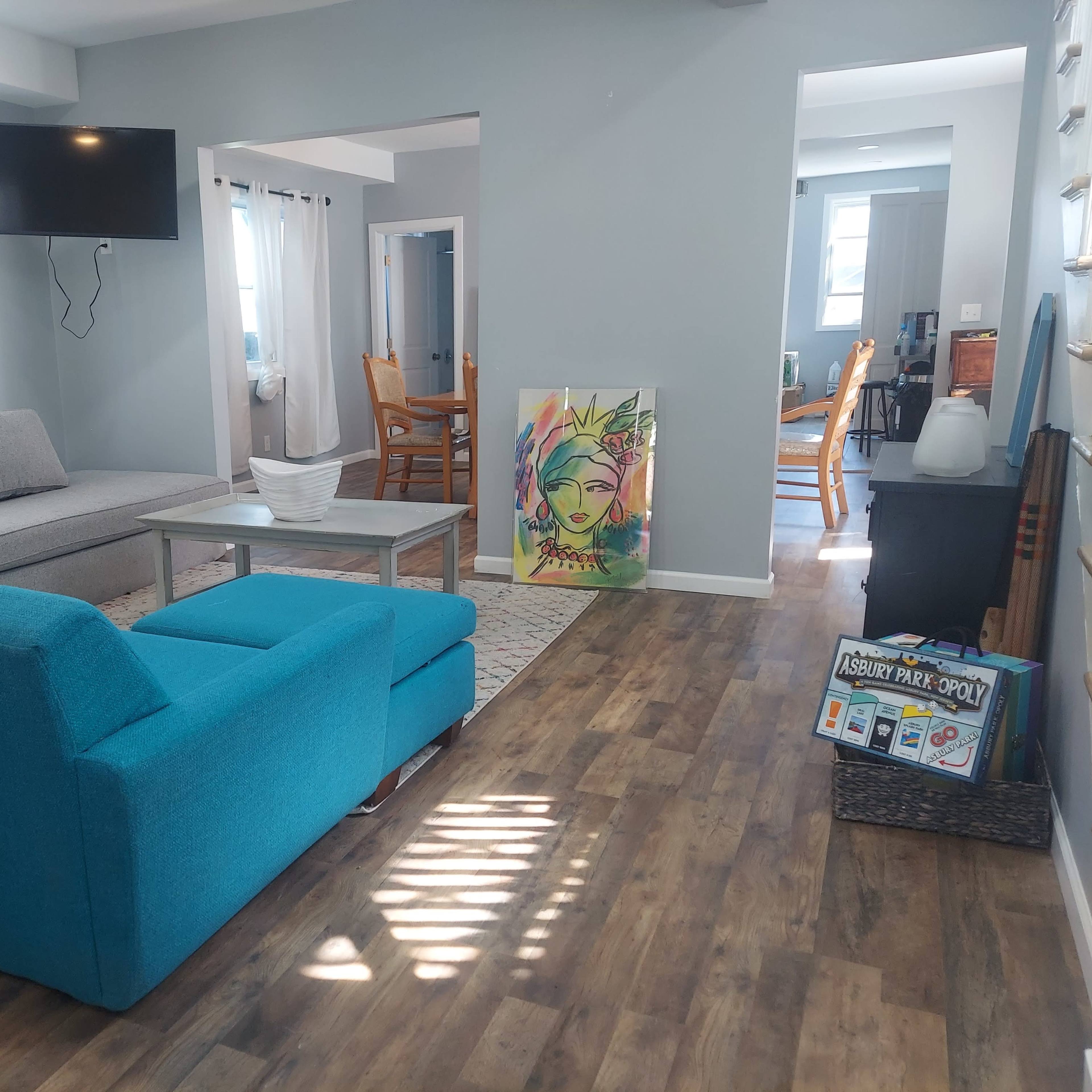 A bright living room with blue and gray furniture, hardwood floors, a television on the wall, and a colorful art piece on display.