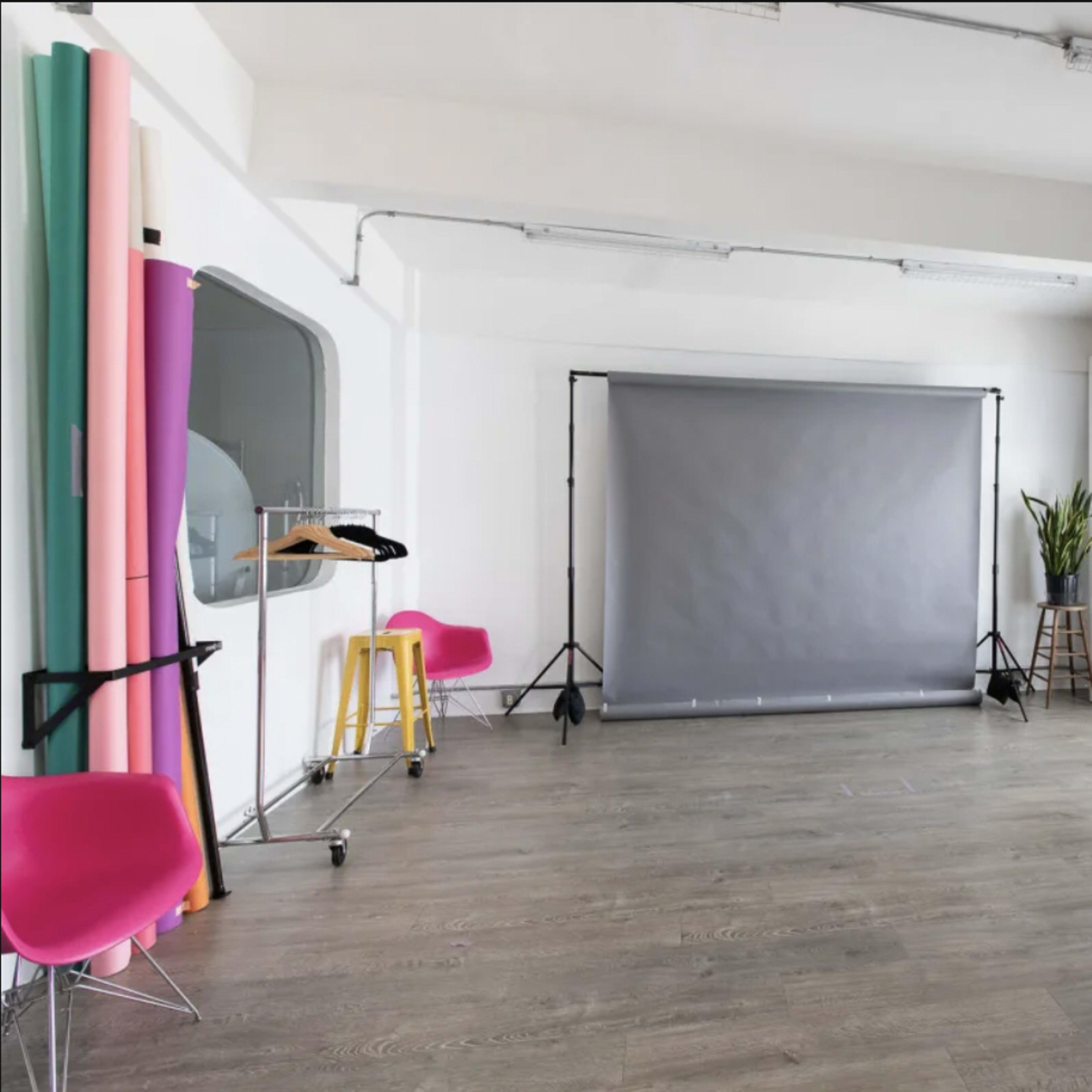 A photography studio featuring a gray backdrop, colorful paper rolls, and a bright window with curtains.