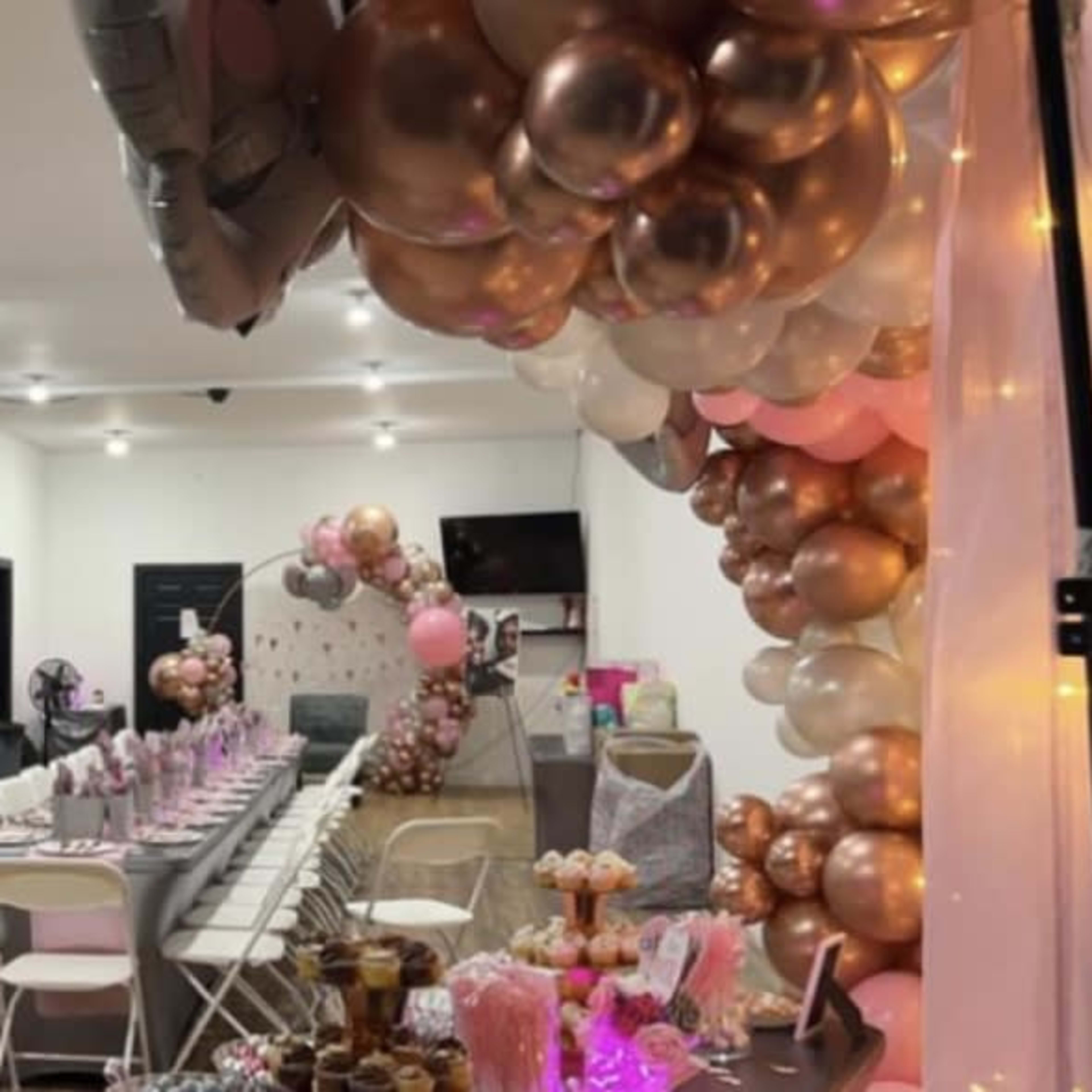 A decorated indoor event space with a long table set for guests and an array of colorful balloons arching over the setting.