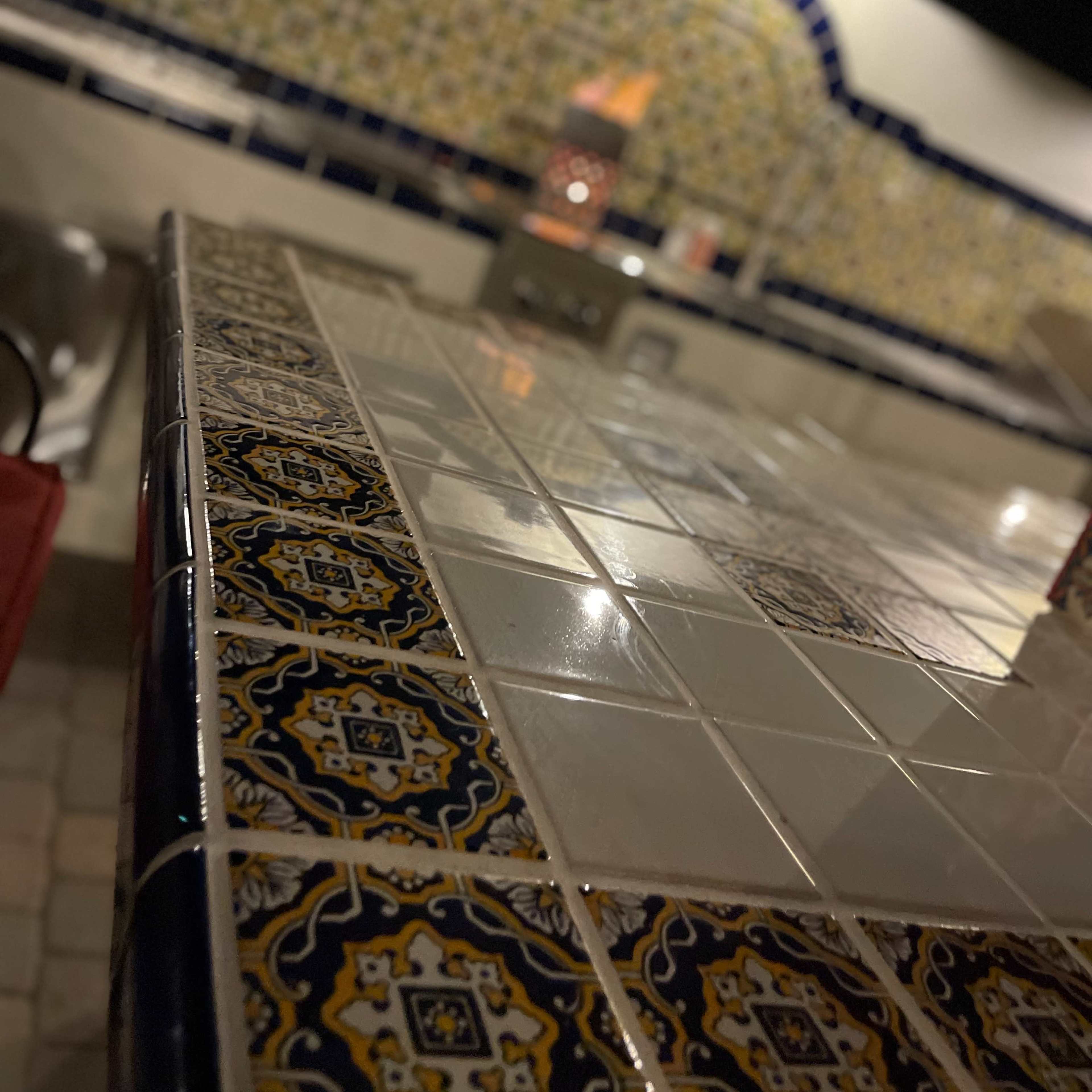 A tiled countertop with a decorative design, set against a patterned tiled wall in a dimly lit space.