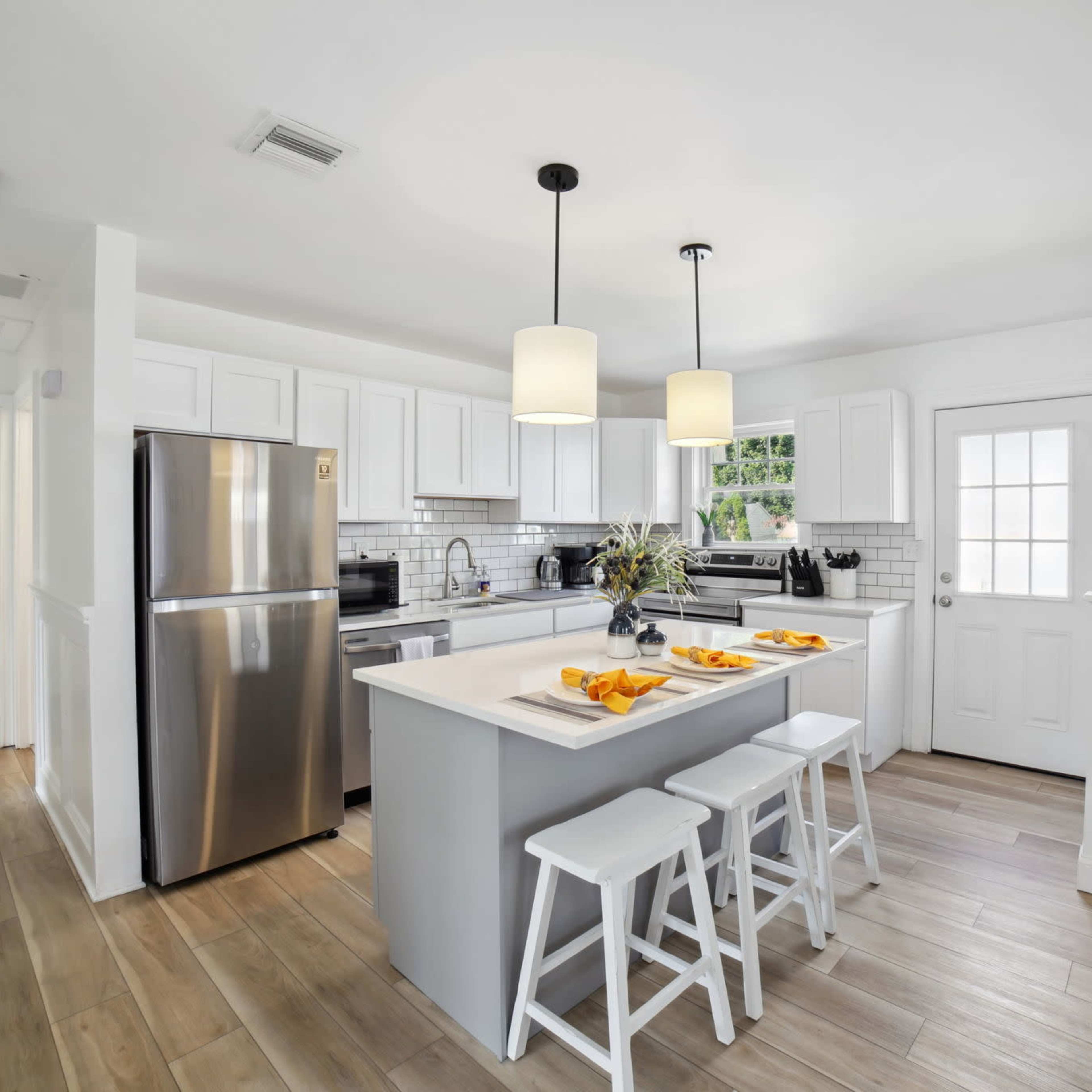 A modern kitchen features white cabinetry, stainless steel appliances, and a centered island with seating for three.