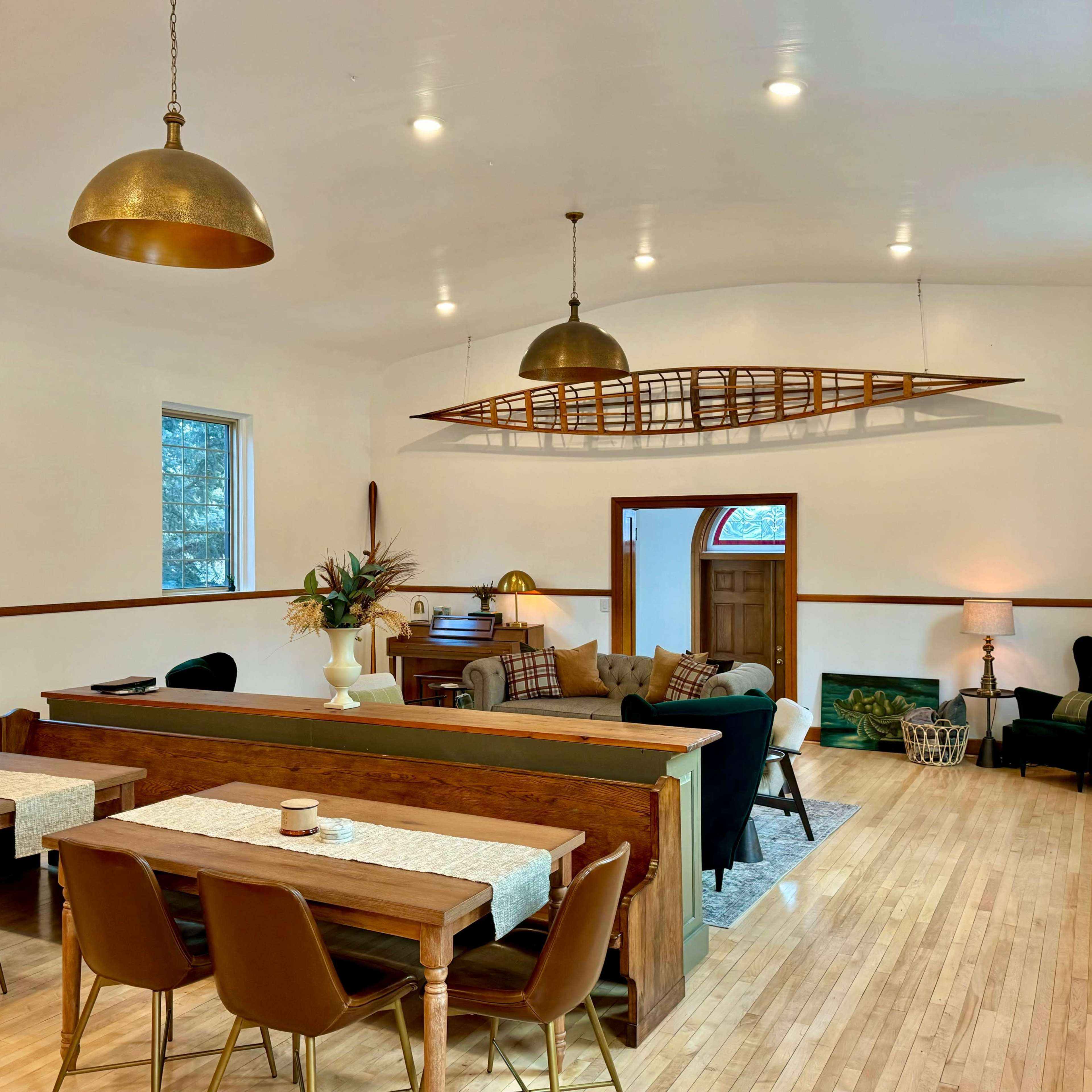 A spacious interior with a dining area featuring wooden tables and chairs, and a cozy living area with a black sofa and a decorative canoe mounted on the wall.