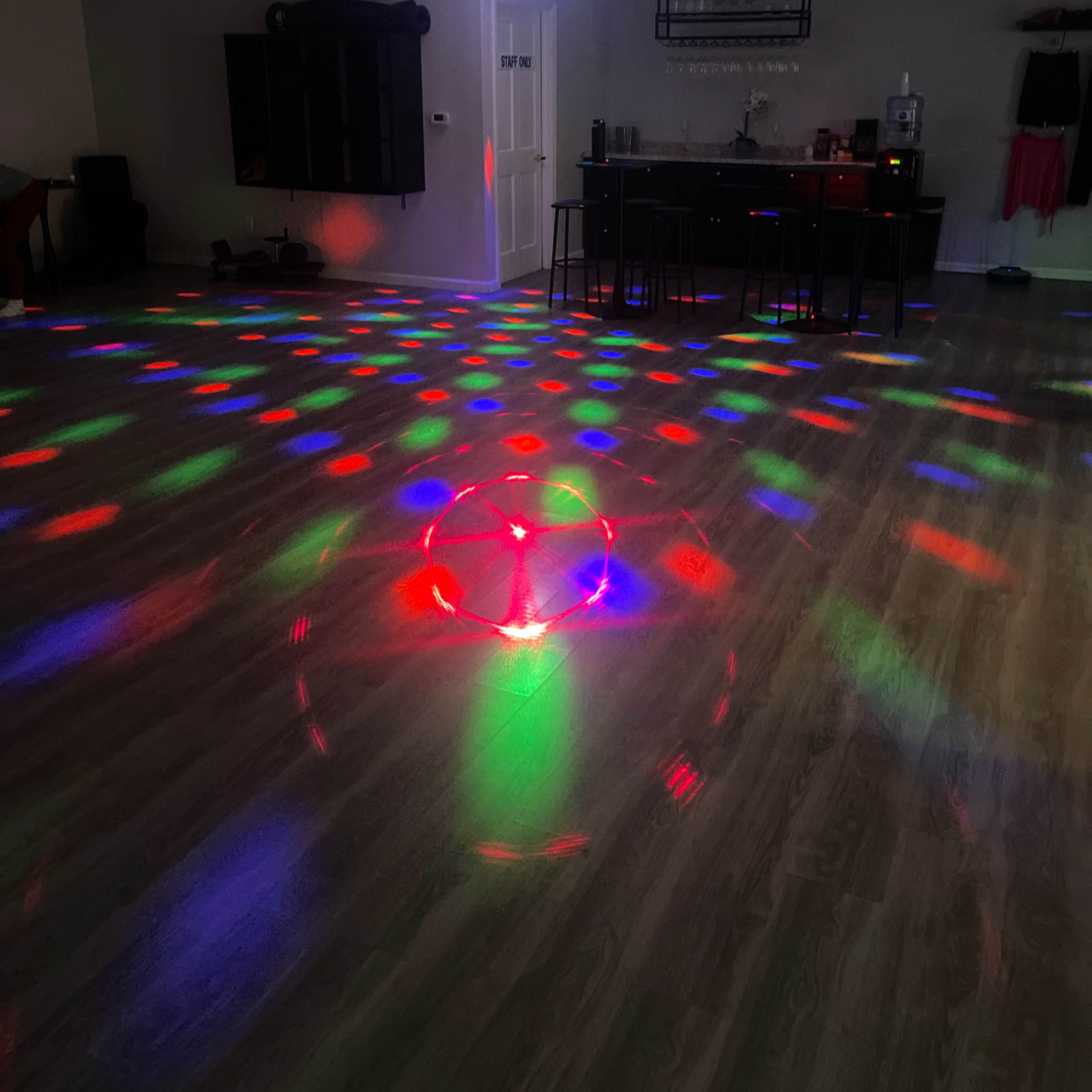 A brightly lit dance studio features colorful lights projecting patterns on the floor and walls.