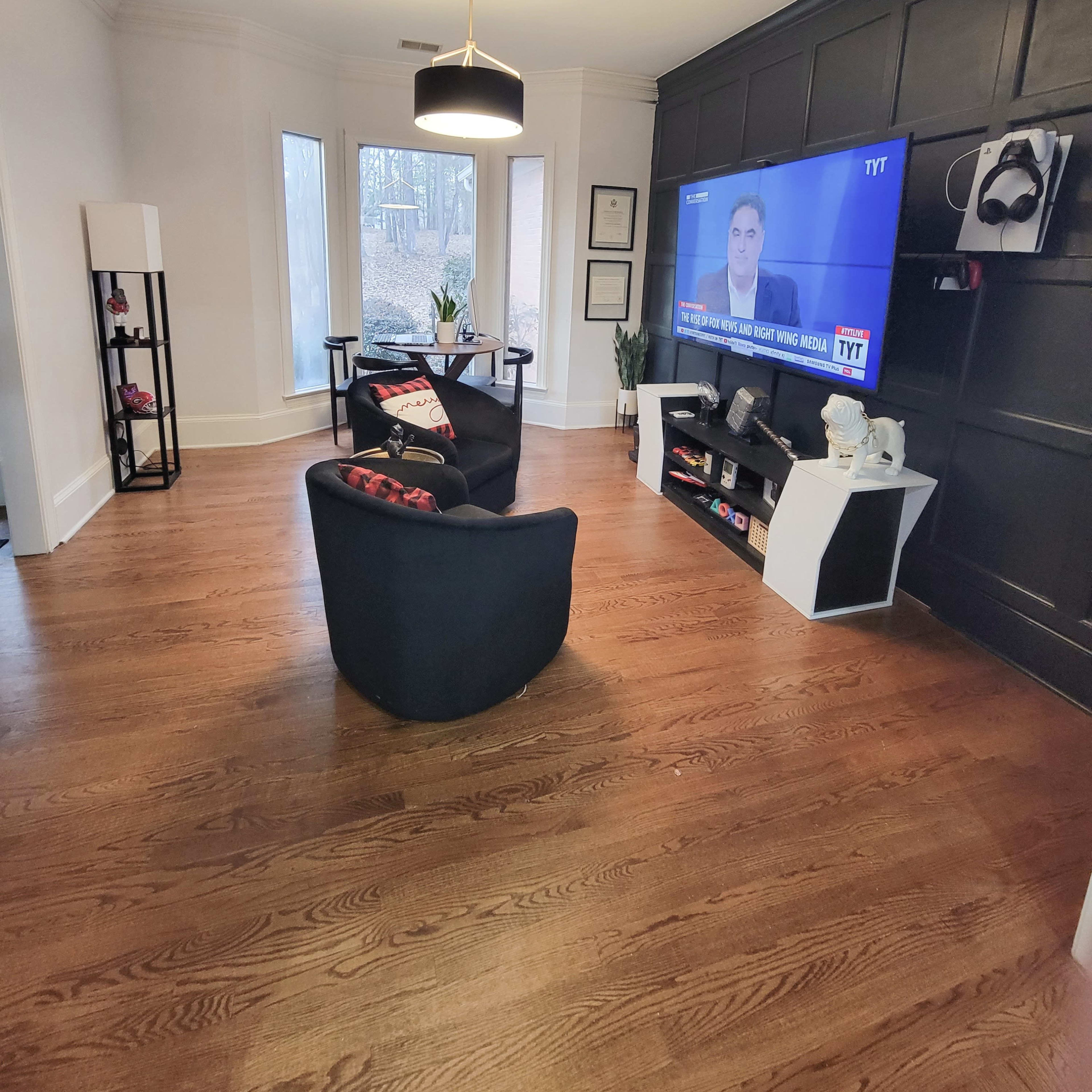 A living room with two black chairs facing a wall-mounted television displaying a news program.