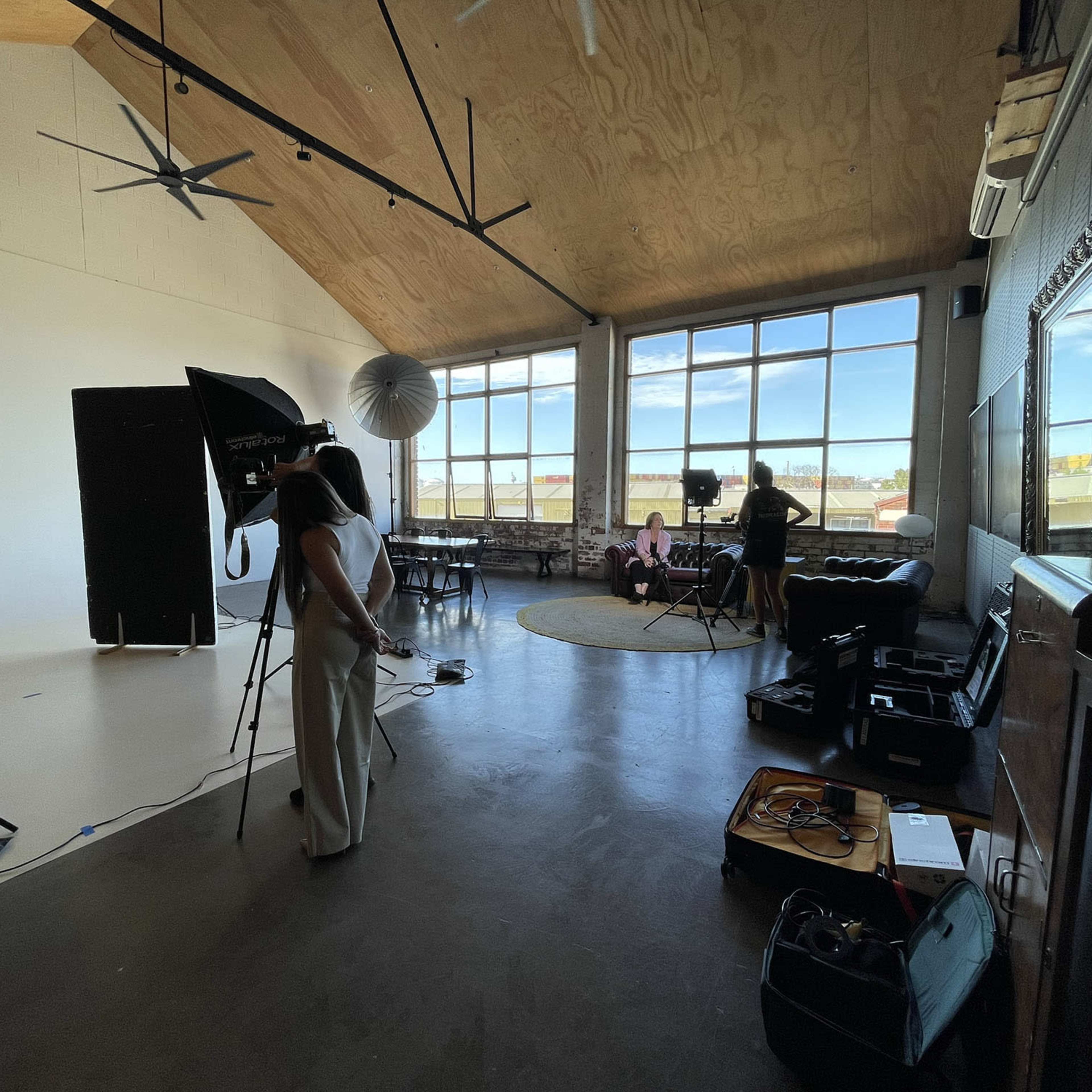 A photography studio features large windows, lighting equipment, and two people preparing for a photoshoot.