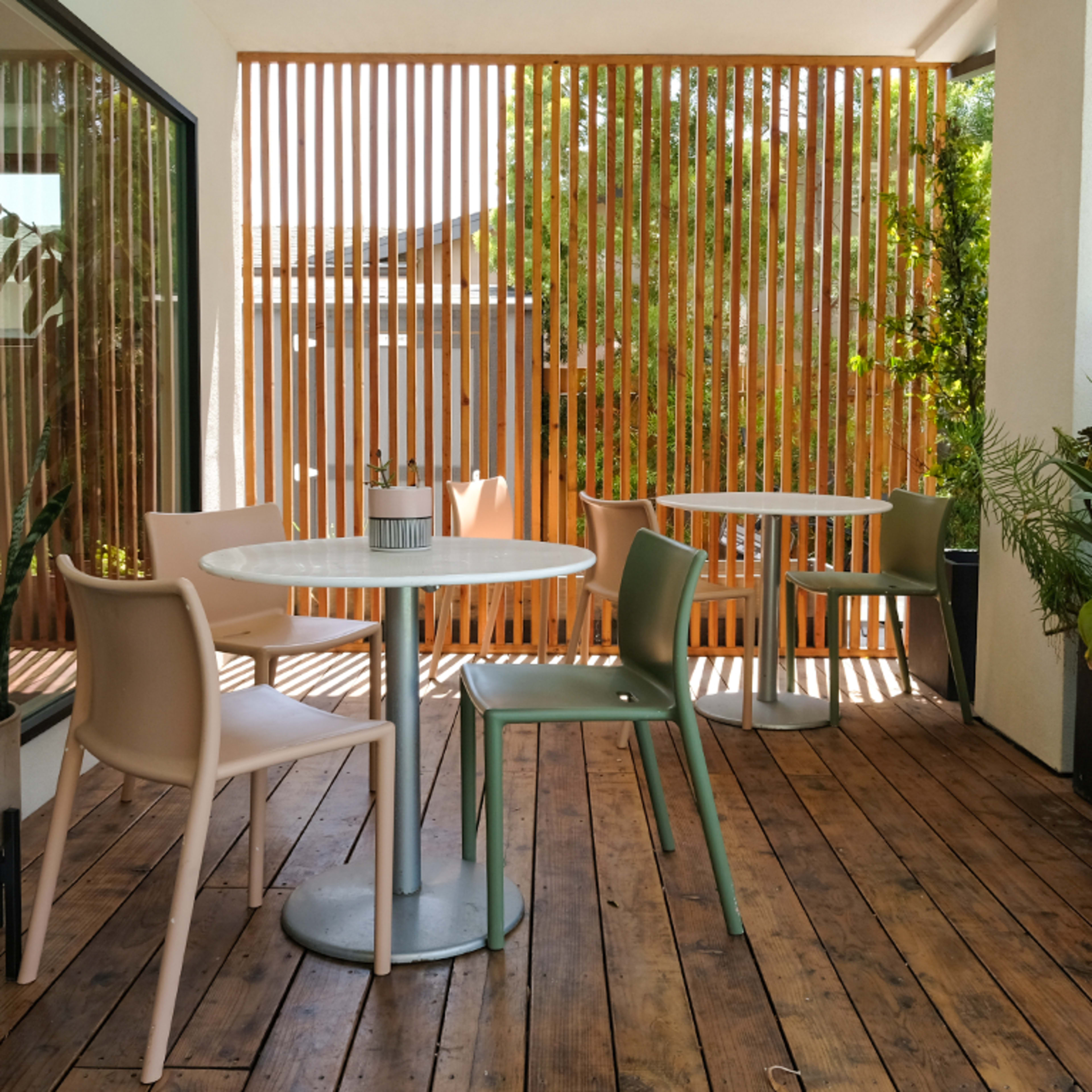 A patio area features two tables with chairs, potted plants, and a wooden slatted divider.