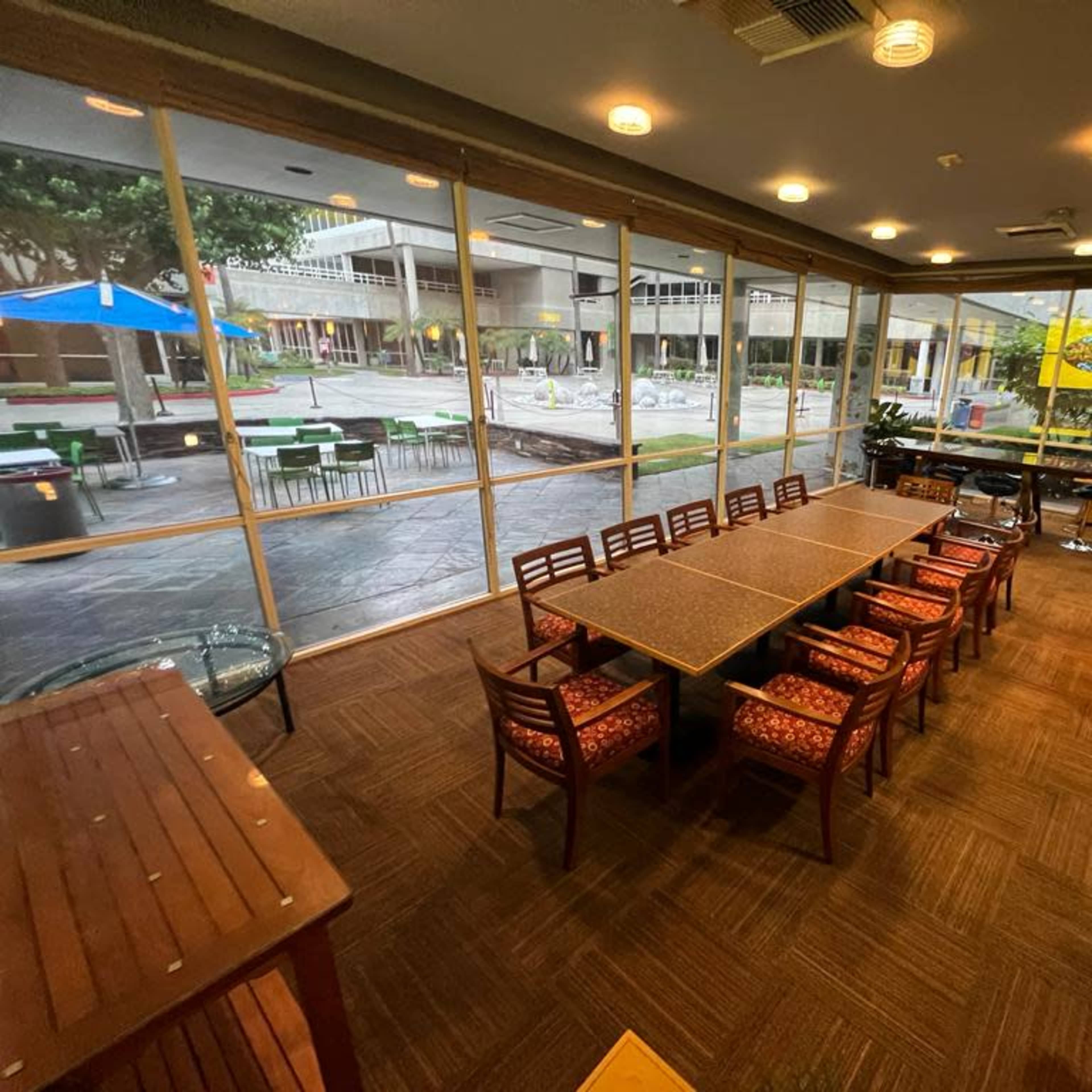 A spacious indoor meeting area with a long table and chairs, overlooking an outdoor courtyard through large glass windows.