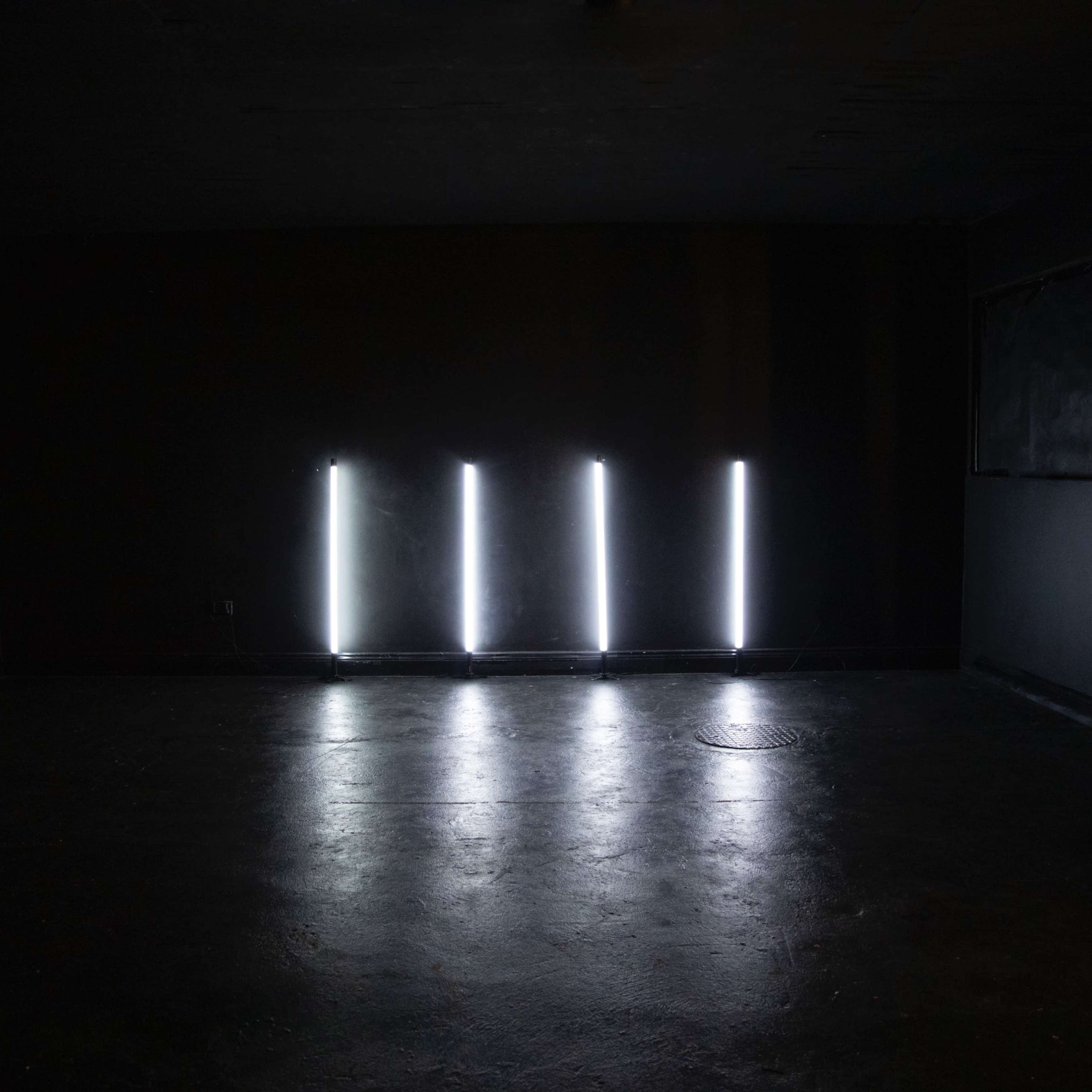 A dimly lit room with four vertical light fixtures illuminating the floor against a dark background.