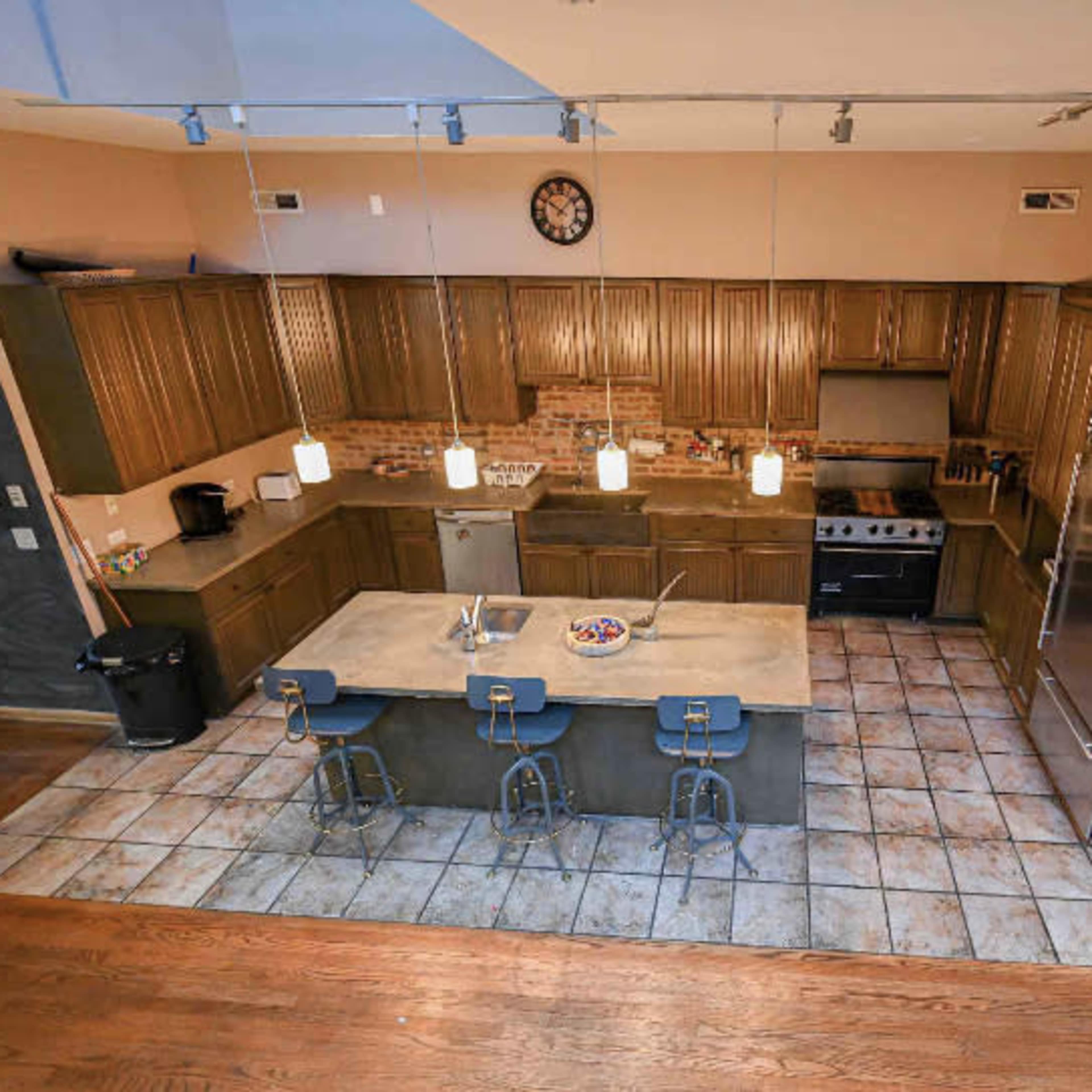 A modern kitchen with wooden cabinets, a large island with seating, and stainless steel appliances, illuminated by pendant lights.