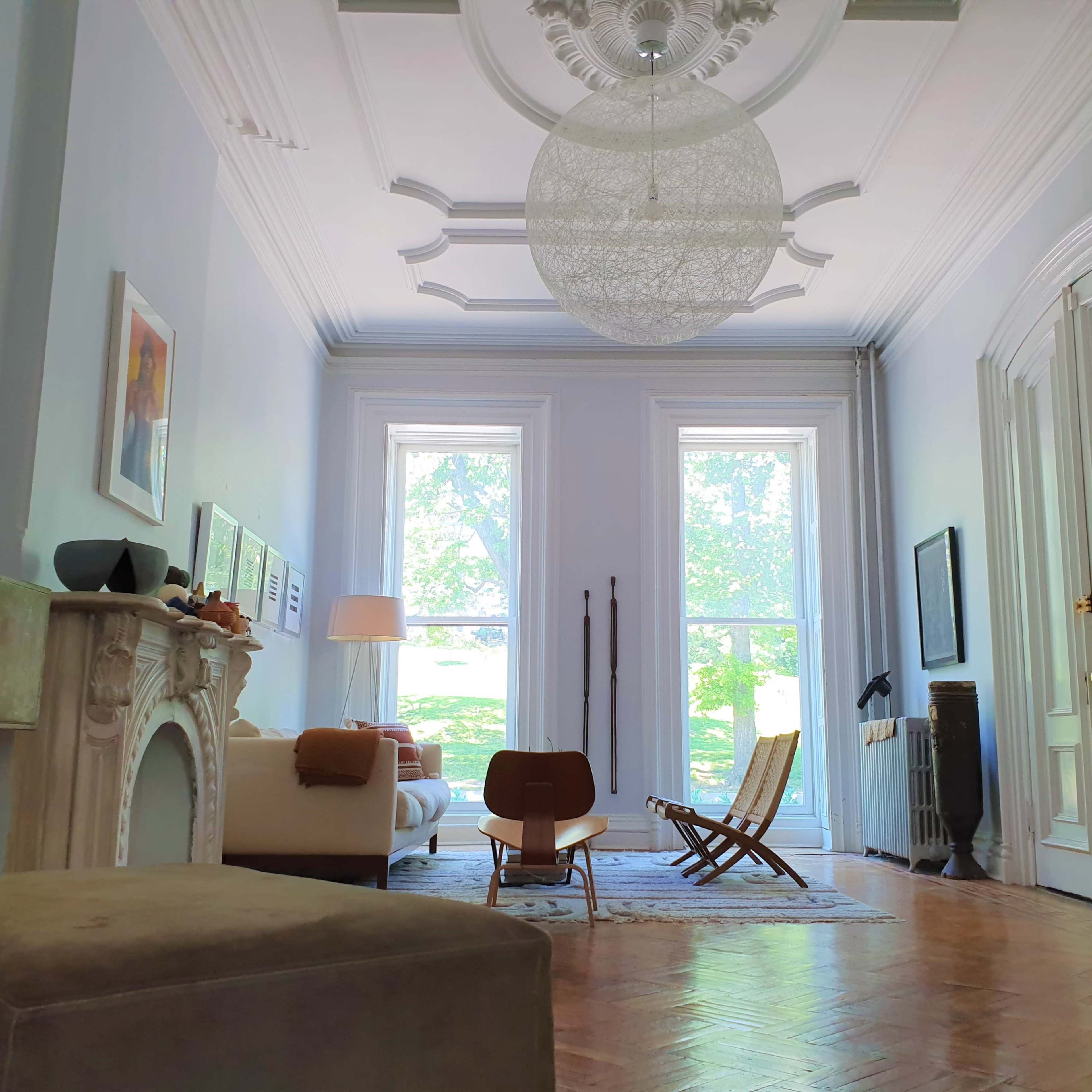 A spacious living room with large windows, a central light fixture, and a mix of modern and classic furniture.