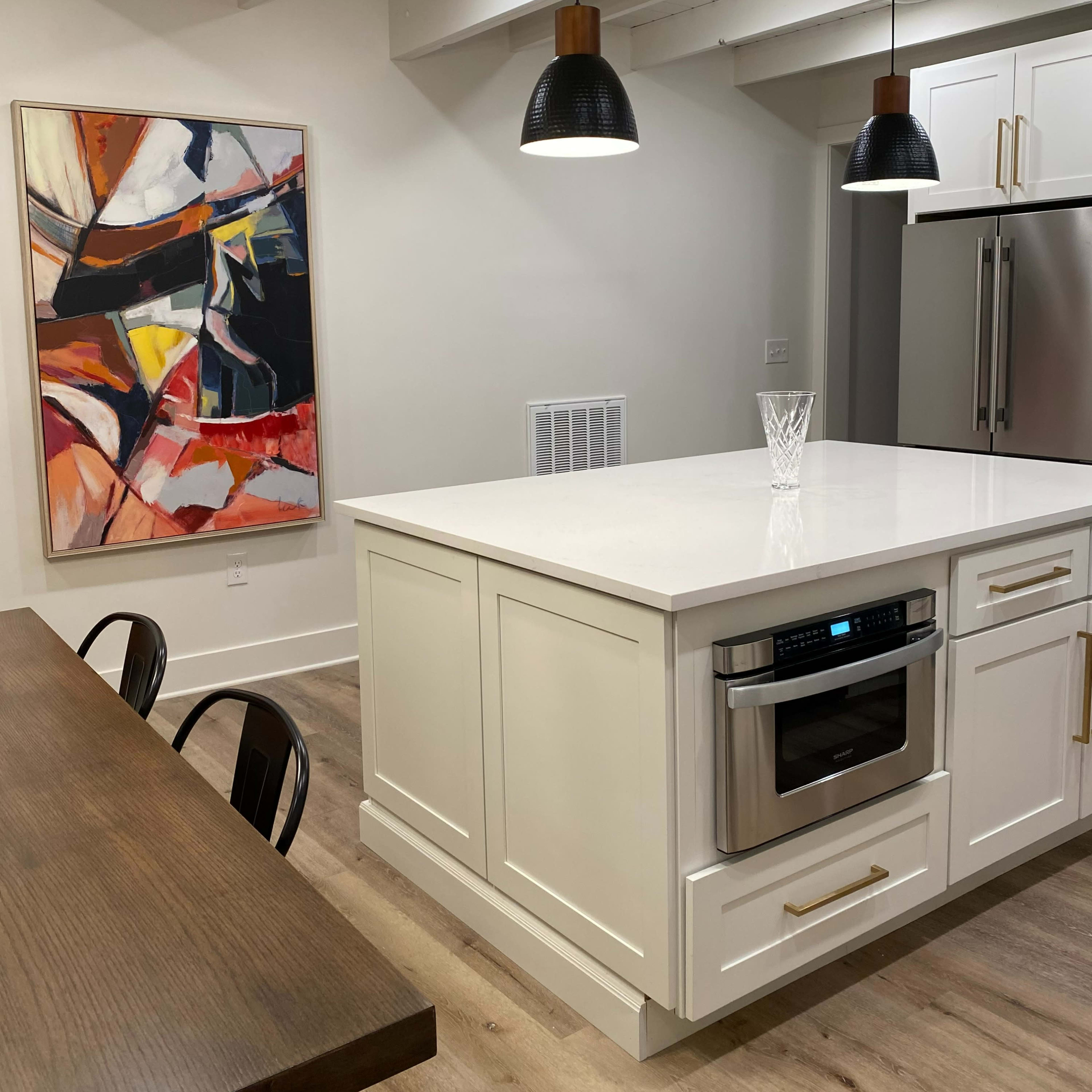 A modern kitchen featuring a large island with an oven, a dining table, and a colorful abstract painting on the wall.