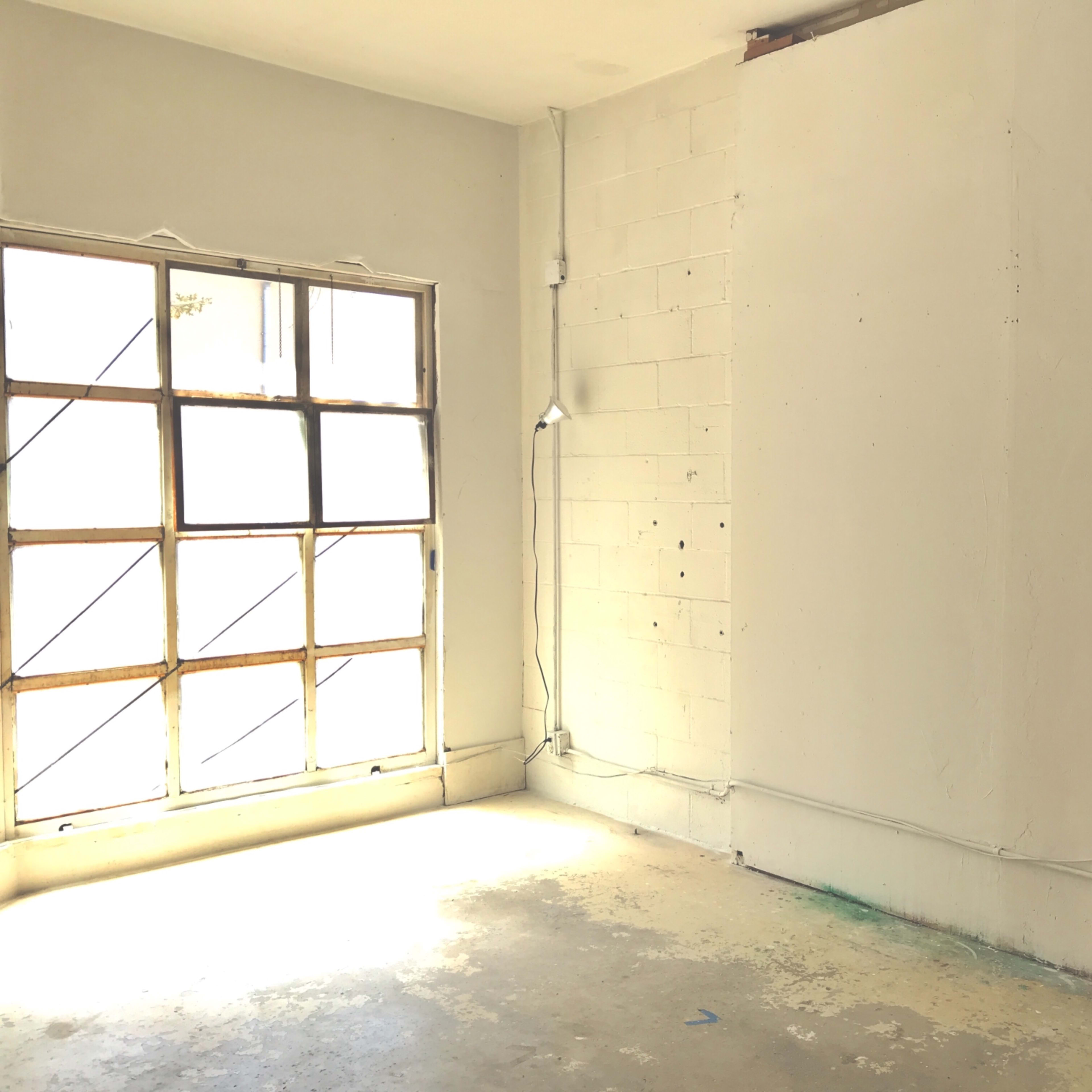 A sparsely furnished room with a large window on one side and bare walls devoid of decorations.