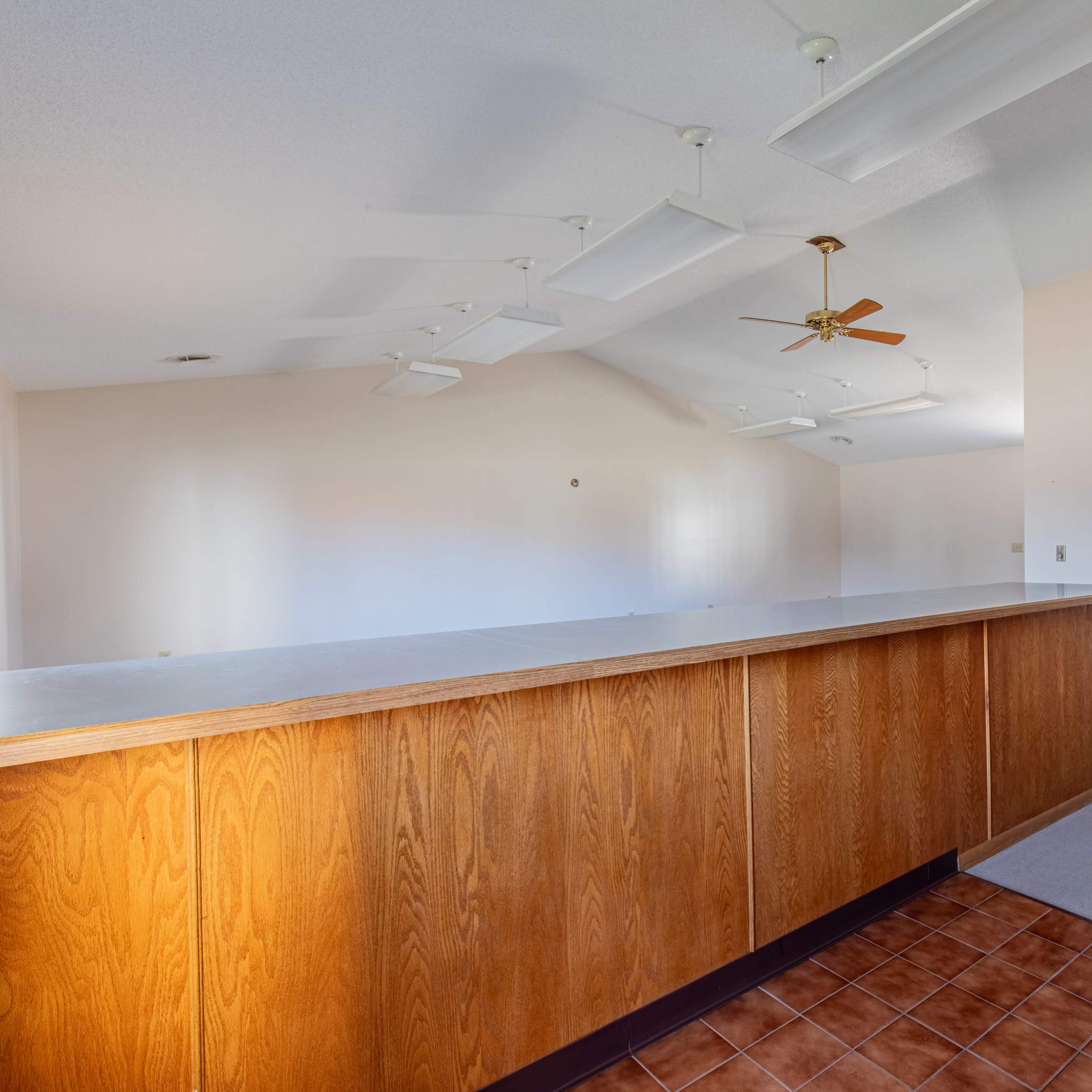 A spacious room with a wooden counter, ceiling fans, and neutral-colored walls.