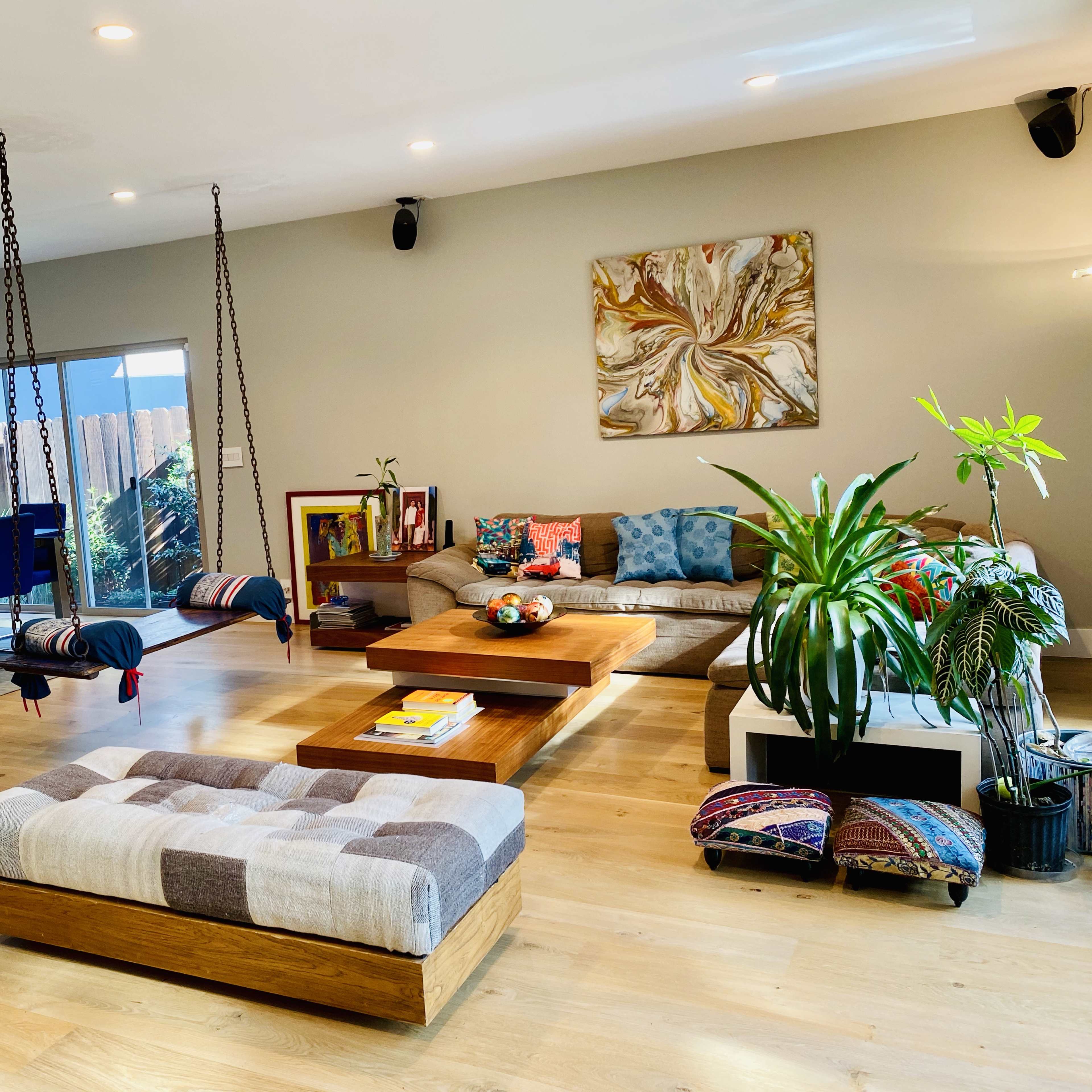 A modern living room with a wooden coffee table, a sectional sofa, two hanging chairs, and a dining area with blue barstools in the background.