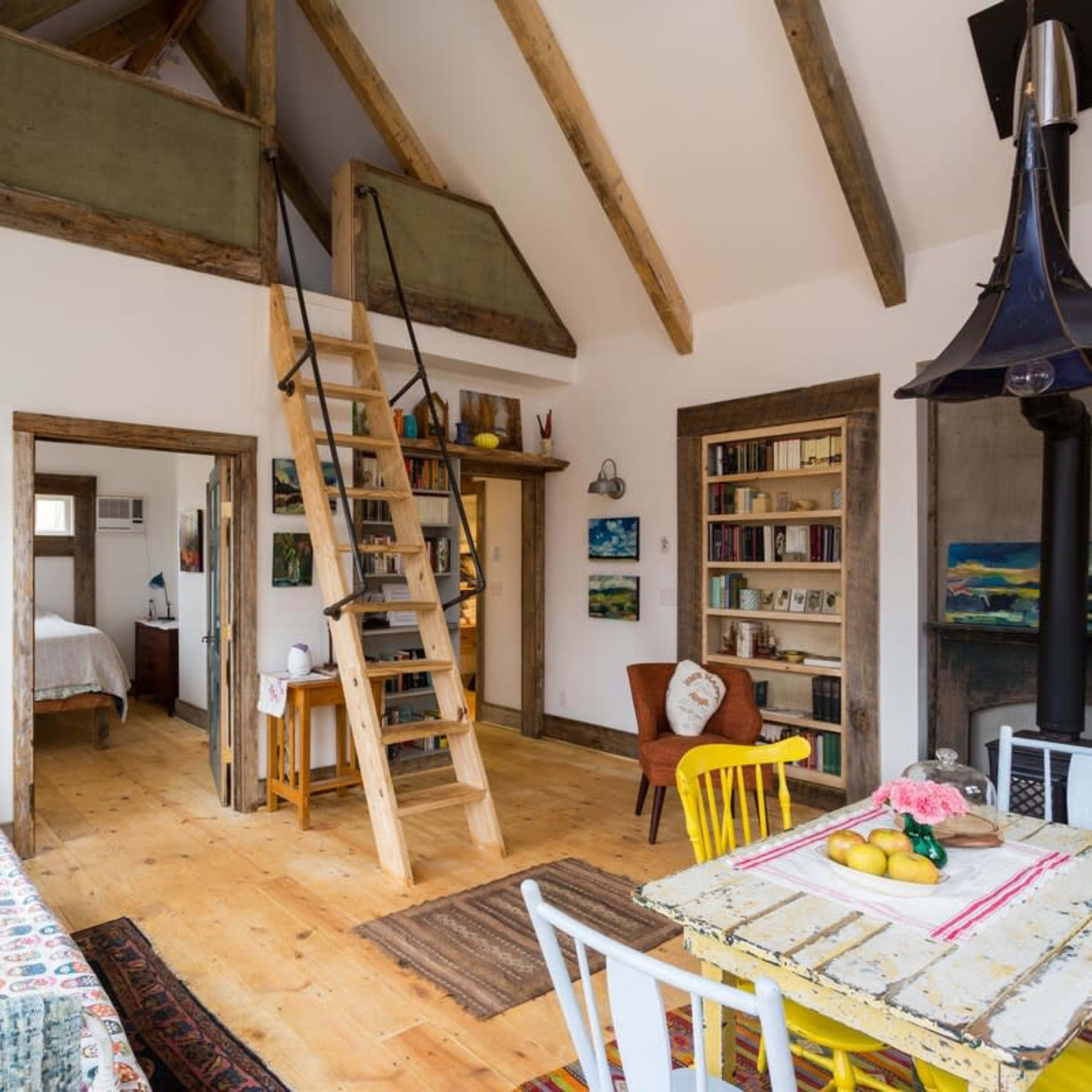 A bright, open-concept living space featuring a kitchen and dining area with a wooden table, colorful chairs, and a staircase leading to a loft.