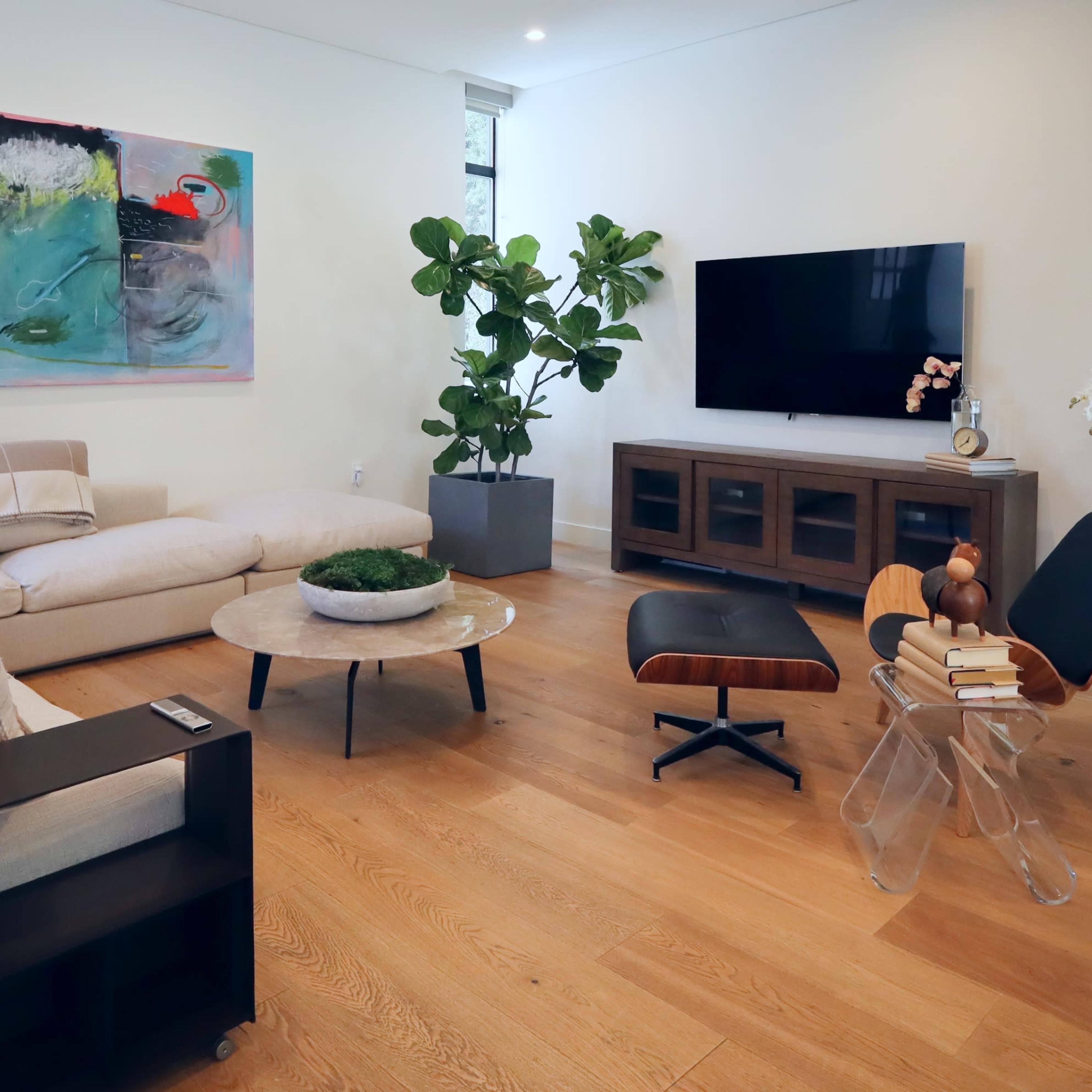 A modern living room with a sectional sofa, a round coffee table, a television mounted on the wall, and a large plant near a side table.