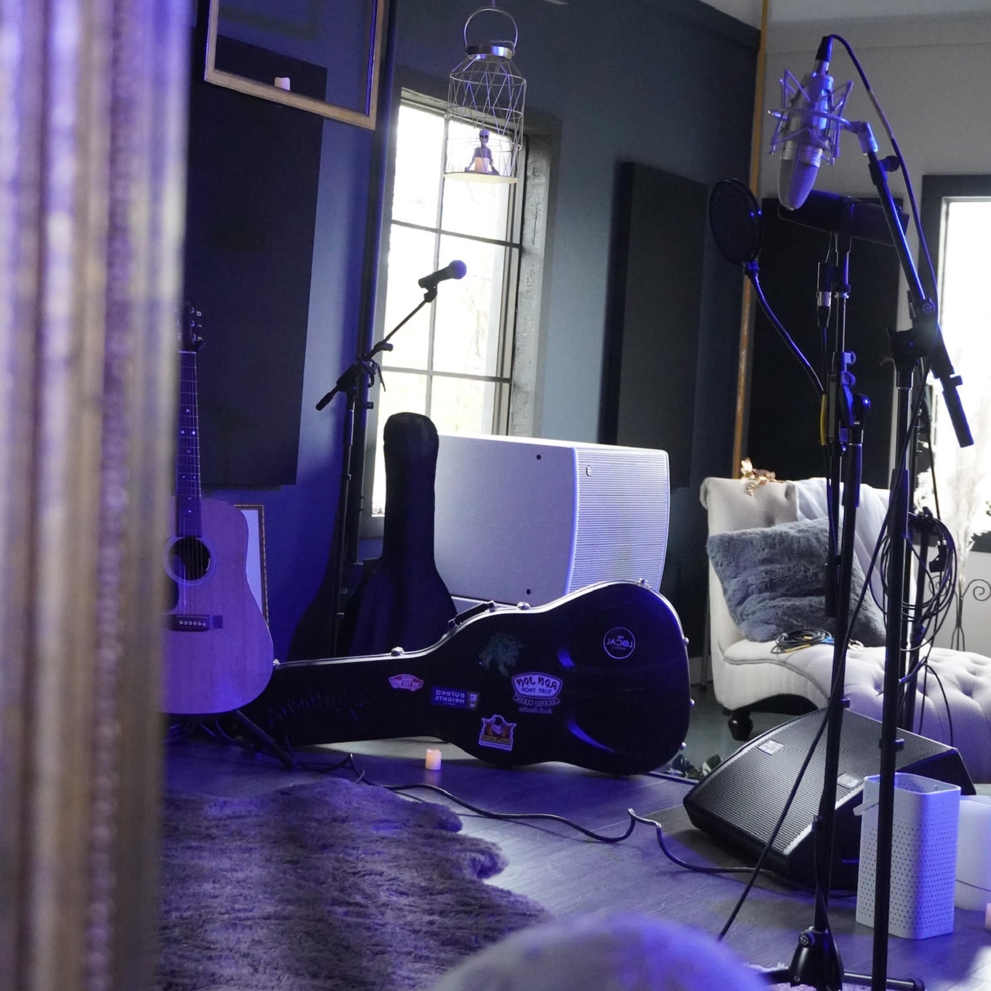 A music studio scene reflected in a mirror, featuring guitars, microphones, and sound equipment arranged in the space.