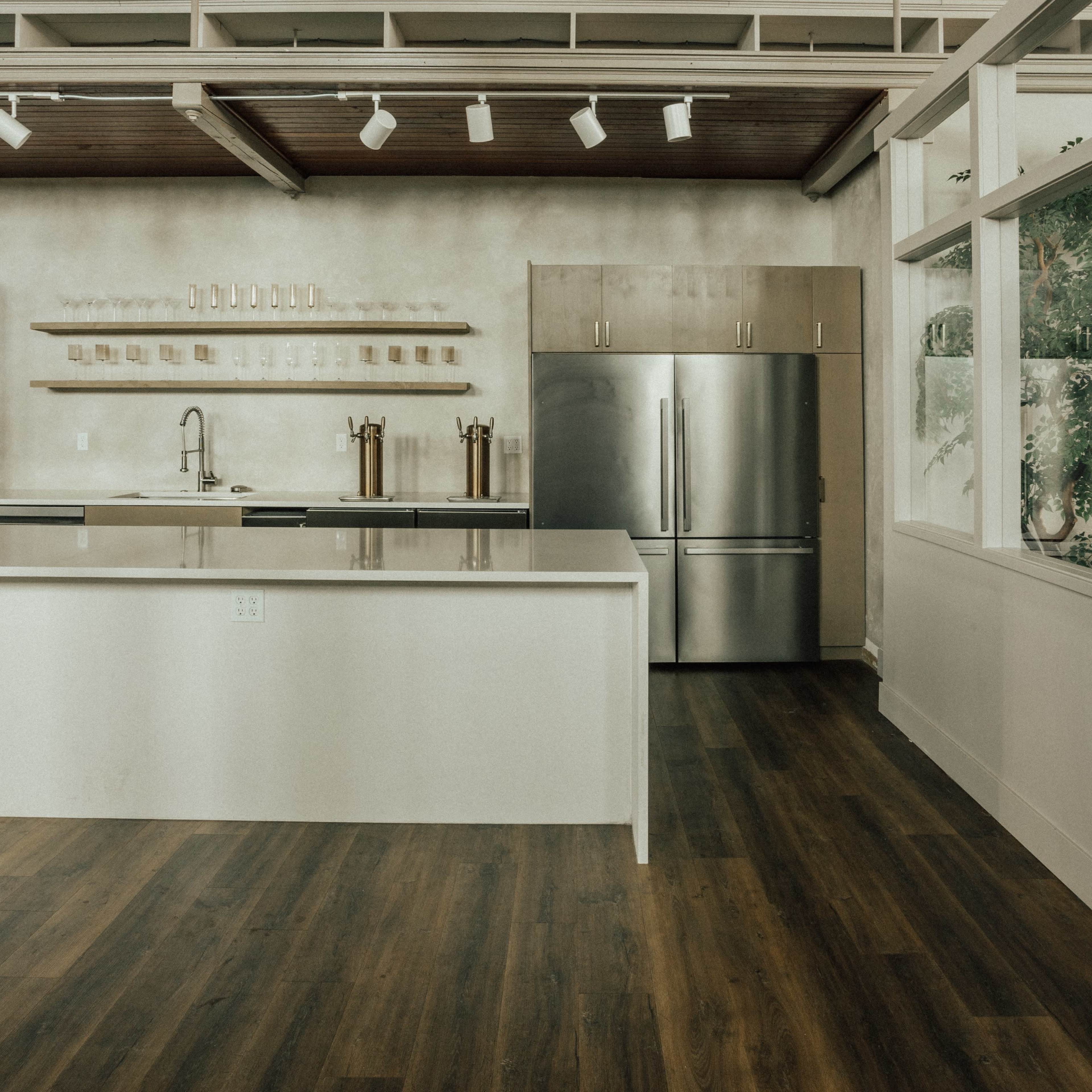 A modern kitchen with a large island, stainless steel appliances, and wooden cabinetry against a light-colored wall.