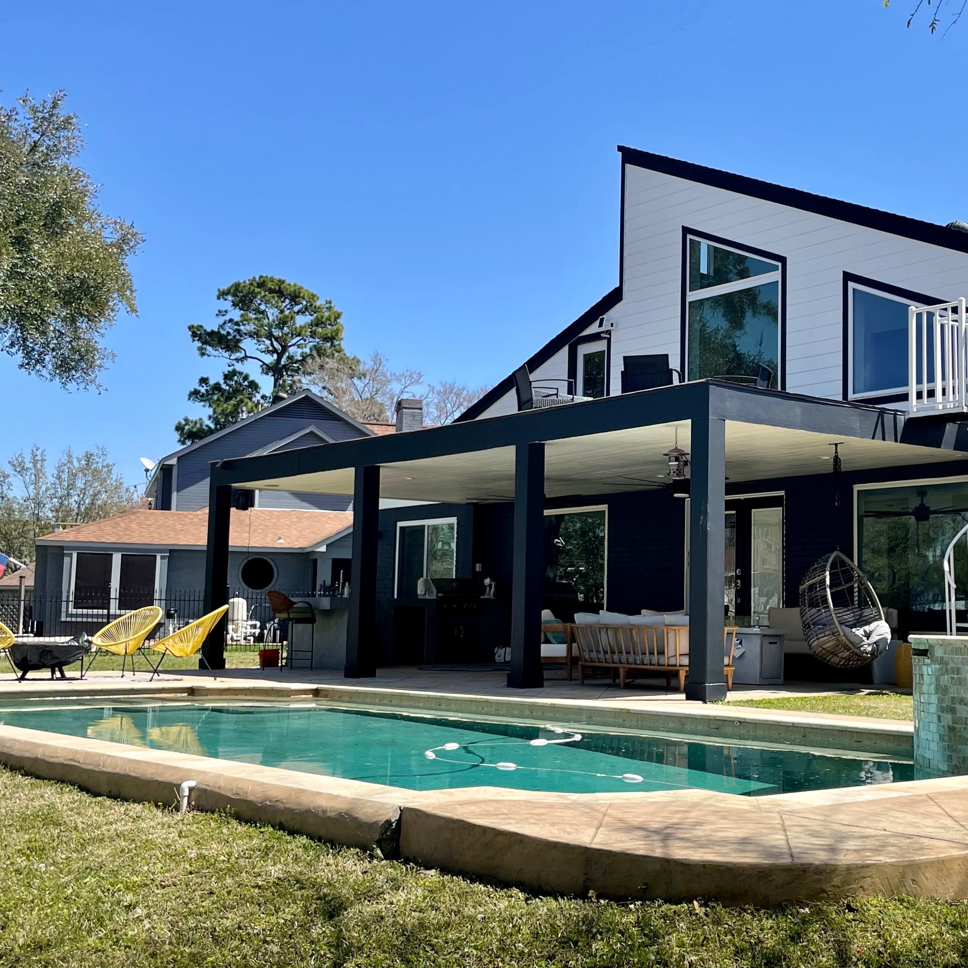 A modern home features a pool, a covered patio area with seating, and a spiral staircase leading to an upper level.